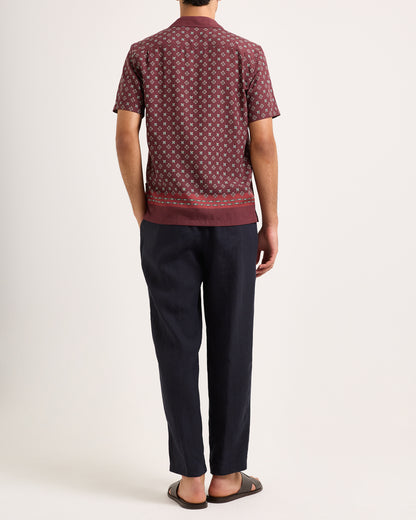 Model wearing maroon short-sleeve shirt with geometric print and navy trousers on a white background