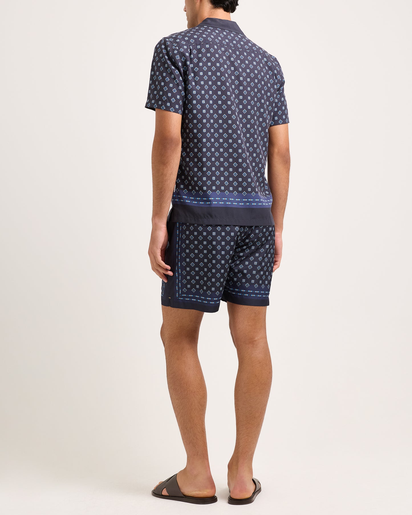 Person wearing a navy patterned shirt and shorts on a white background