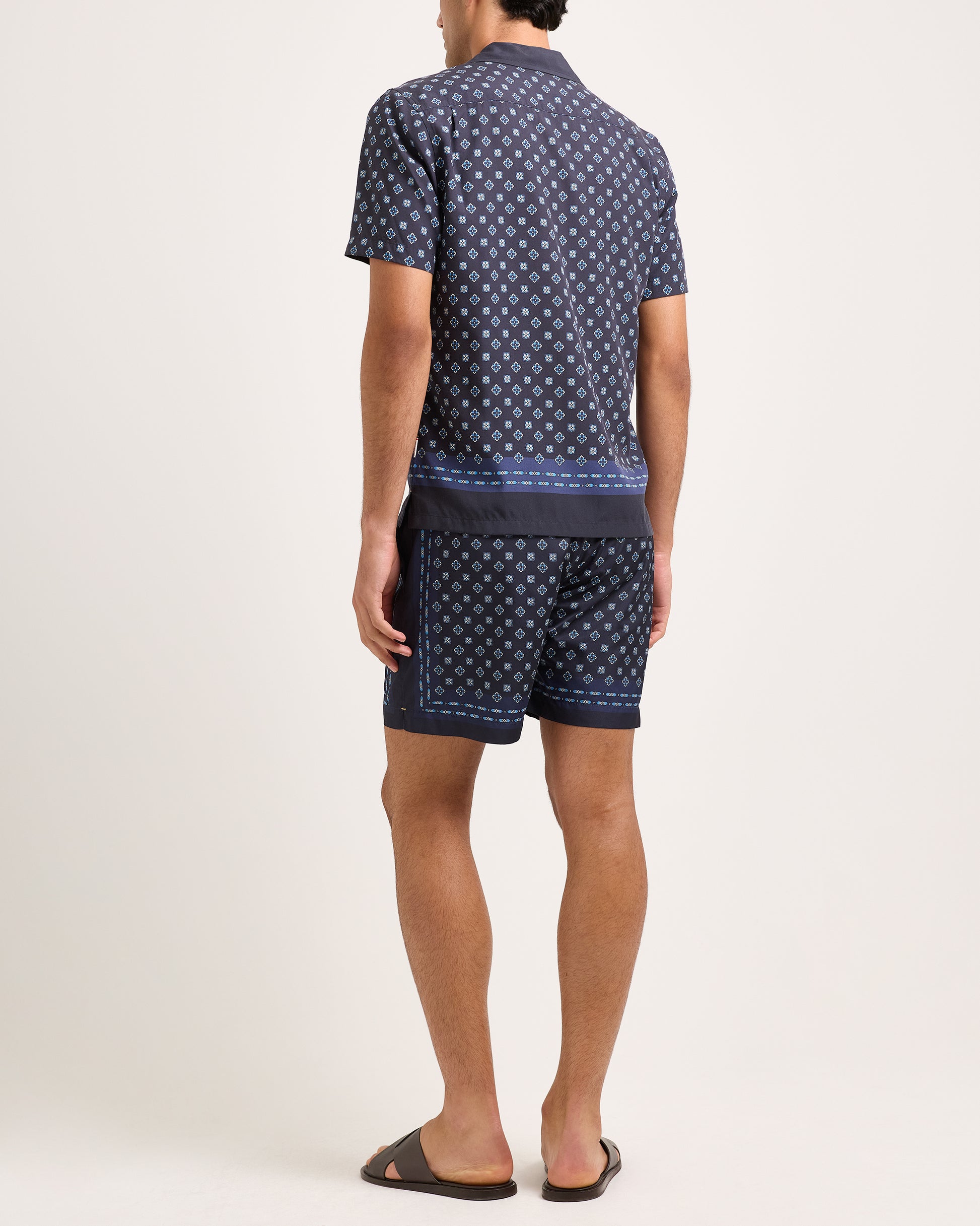 Person wearing a navy patterned shirt and shorts on a white background