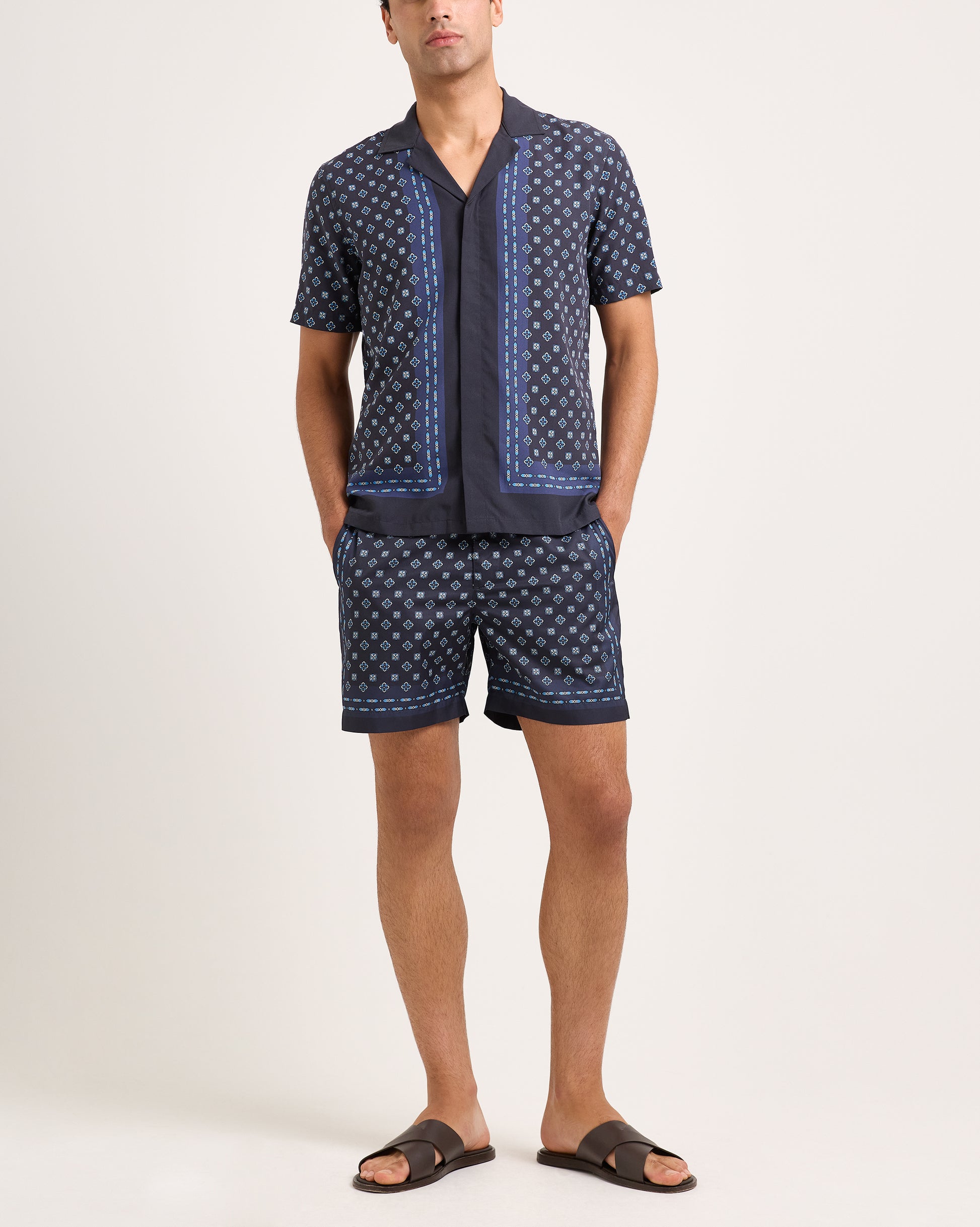 Man wearing a navy patterned shirt and shorts set on a white background
