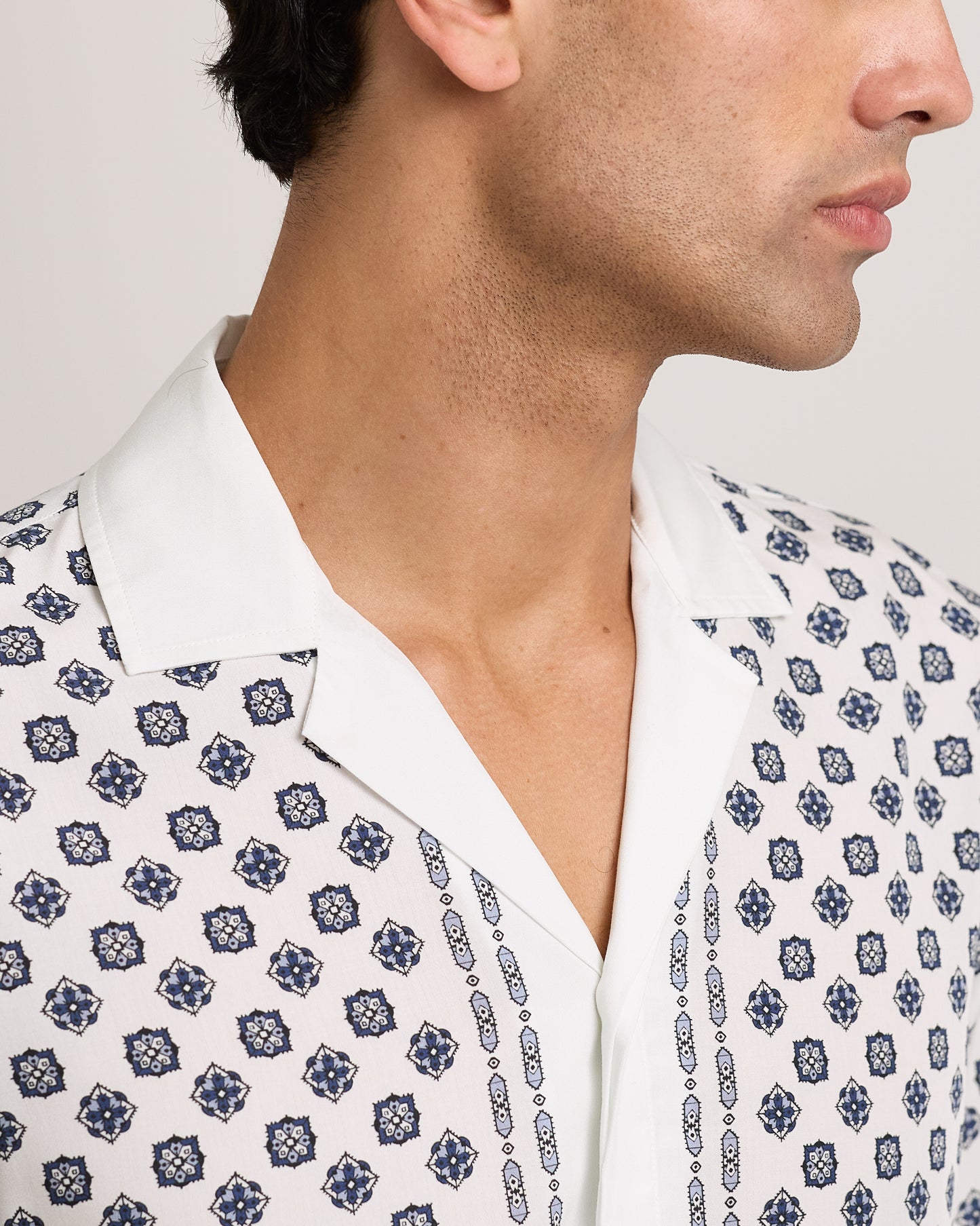 Close-up of model wearing short-sleeve shirt with a black geometric pattern on a white background