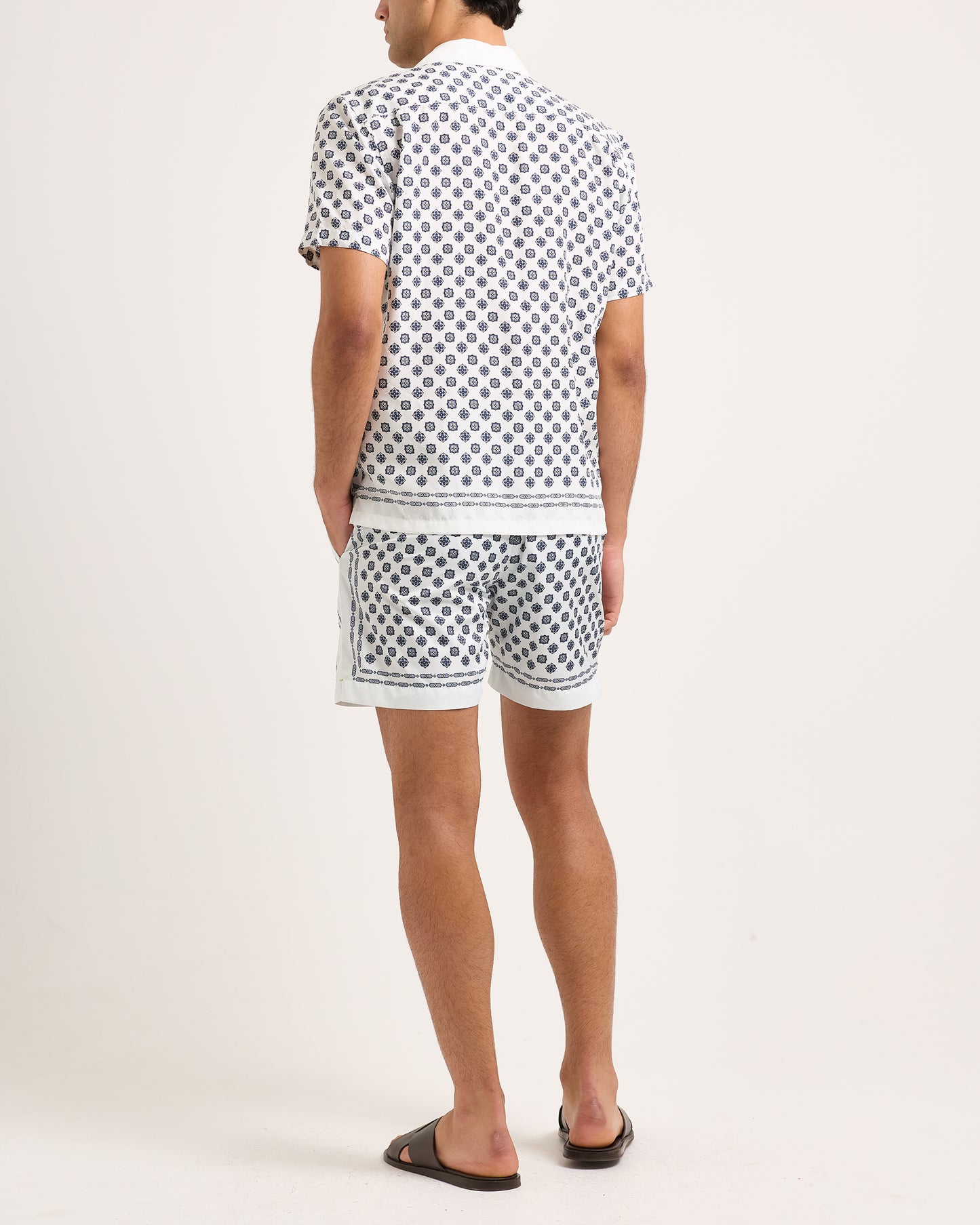 Model wearing short-sleeve shirt with a black geometric pattern and matching shorts on a white background