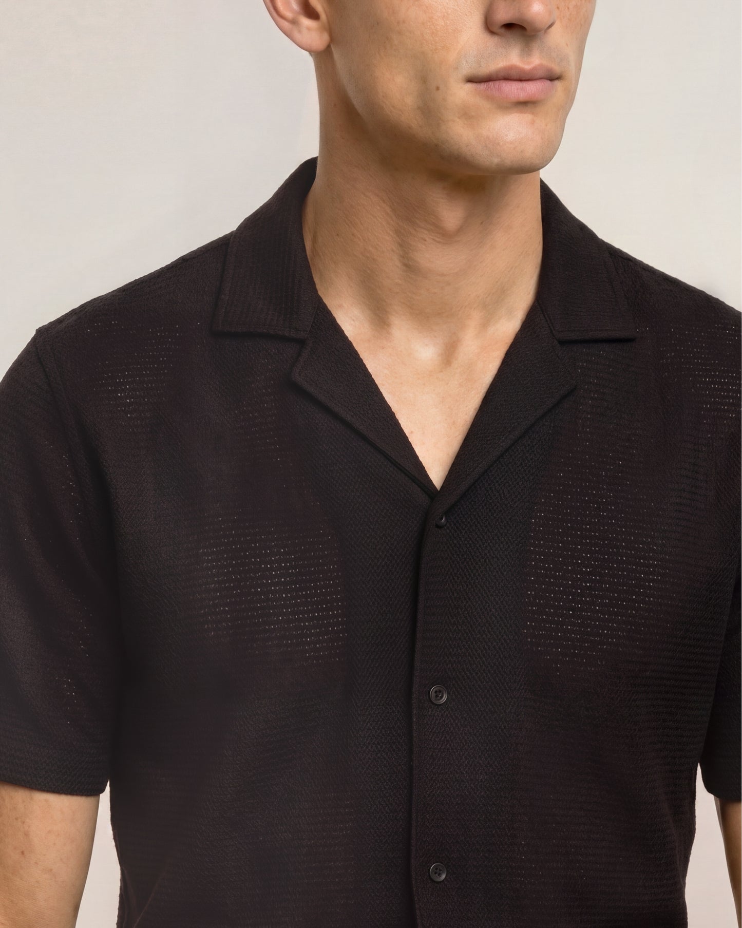 Man wearing a textured black shirt against a neutral background