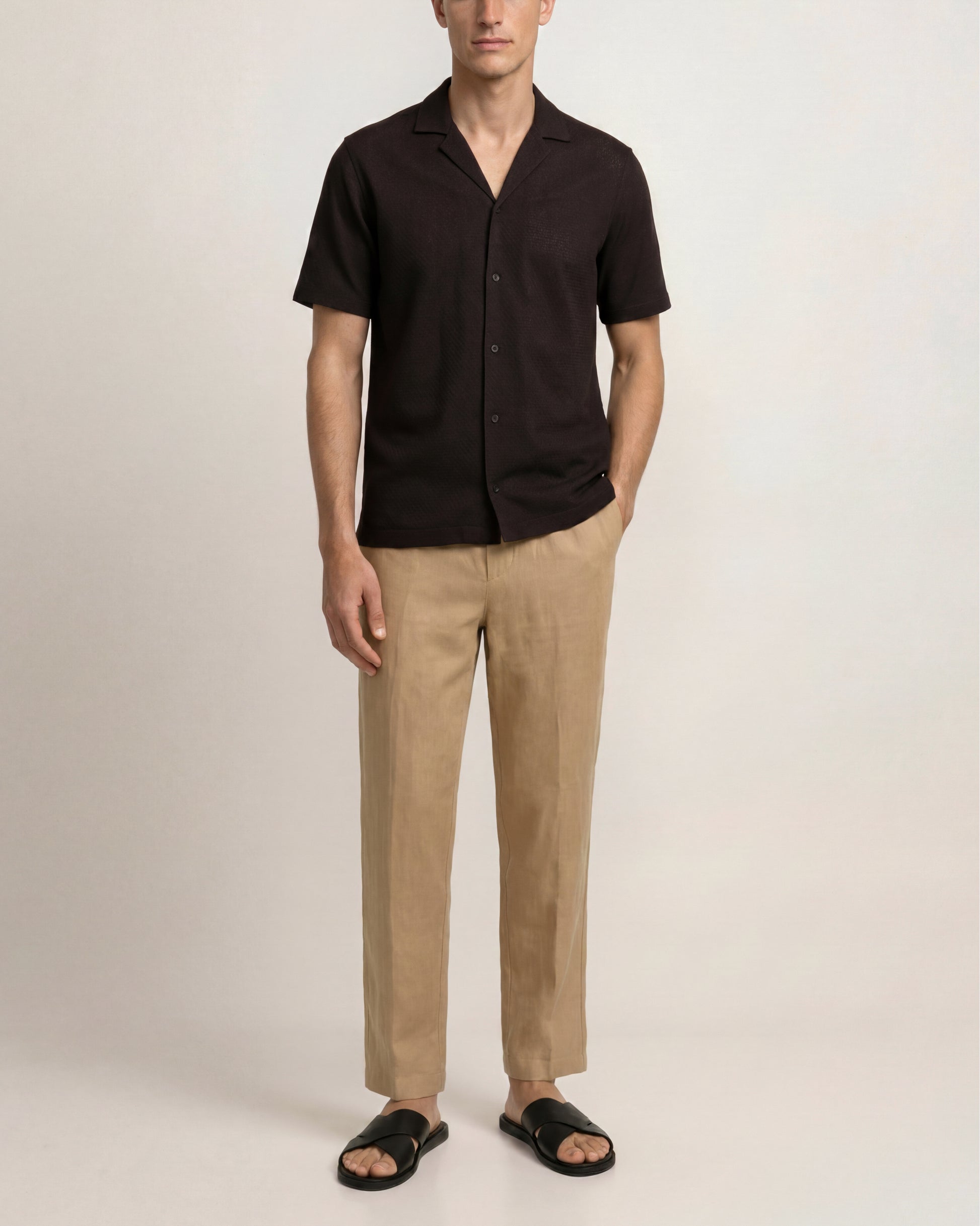 Man wearing a black shirt and beige pants on a plain background