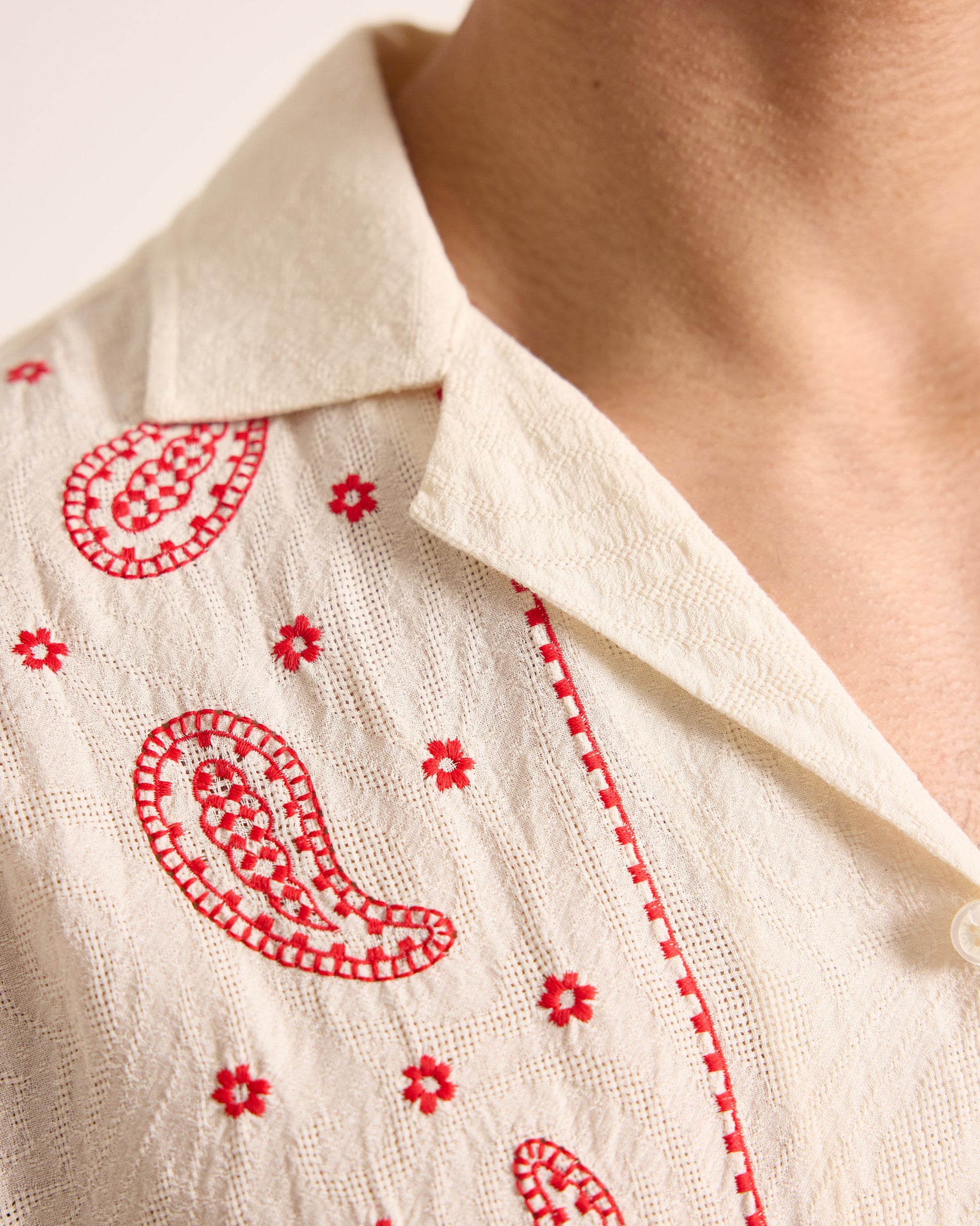 Close-up of a beige shirt with red embroidery on a neutral background