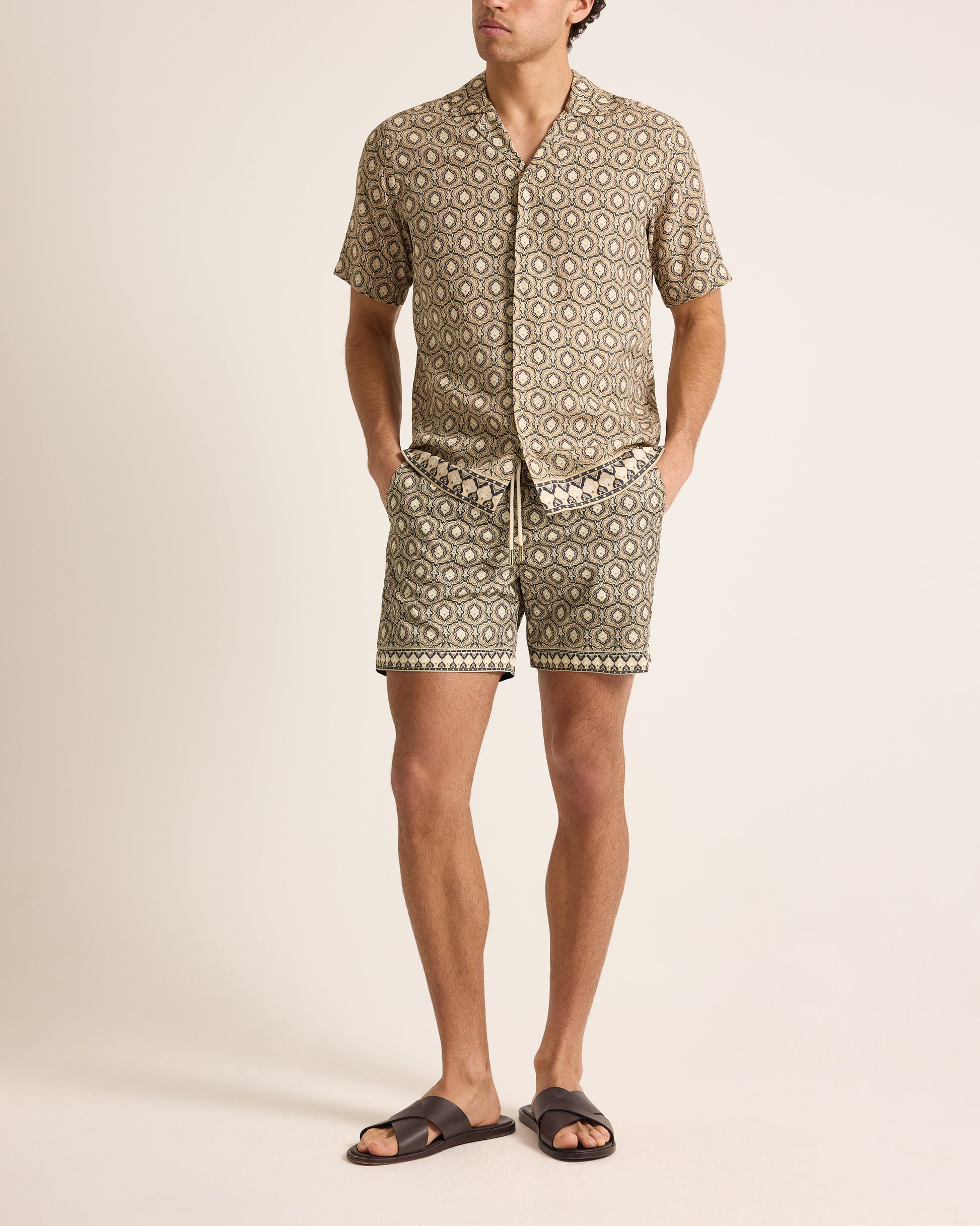 Man wearing a patterned shirt and shorts set on a beige background