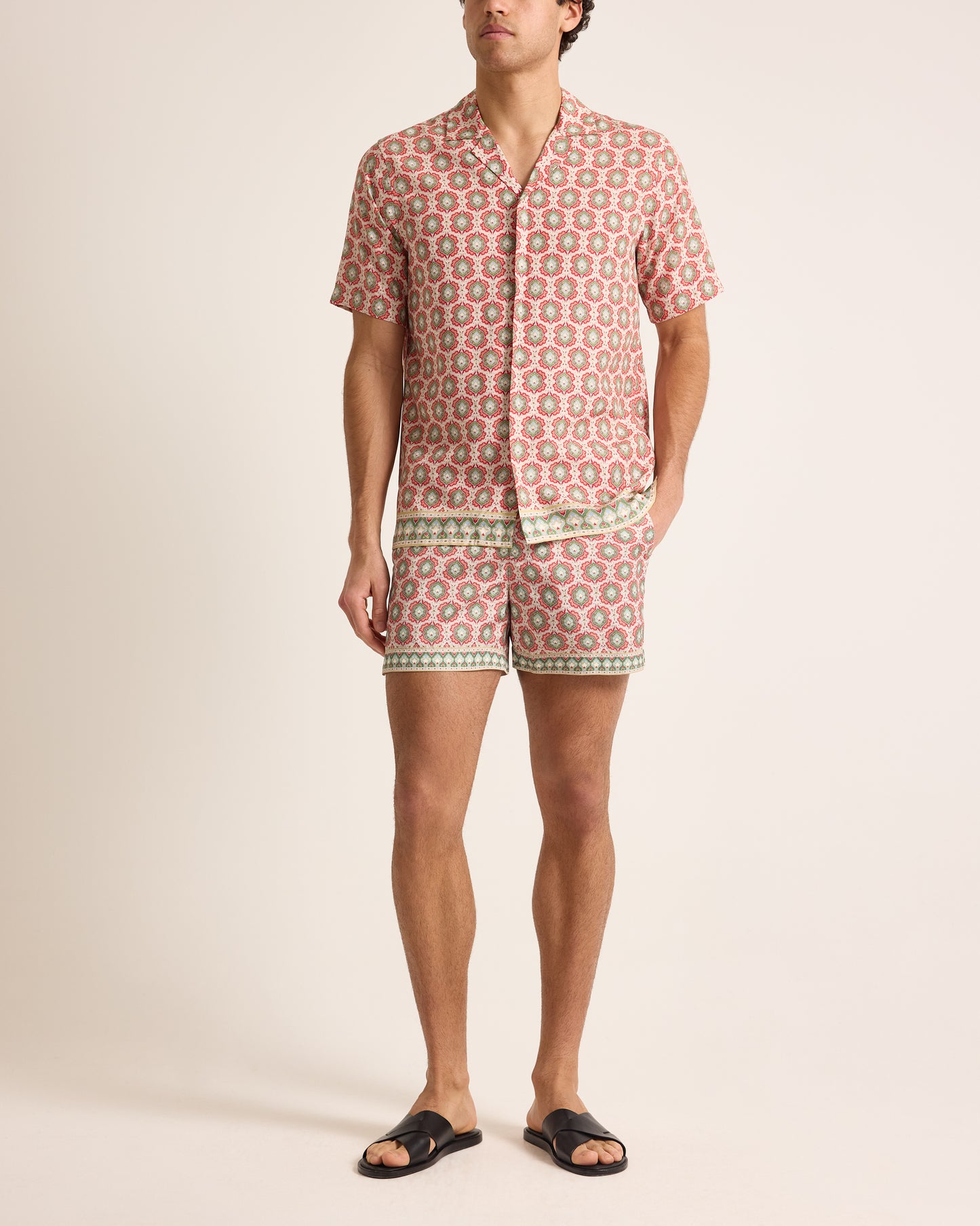 Man wearing a patterned shirt and shorts on a plain background