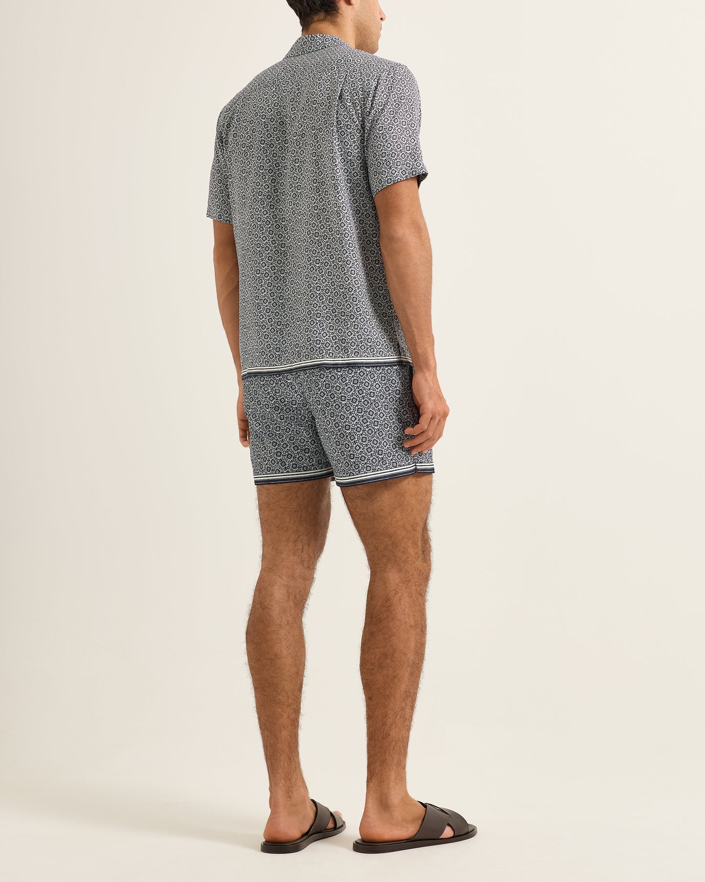 Man wearing a patterned shirt and shorts on a plain background