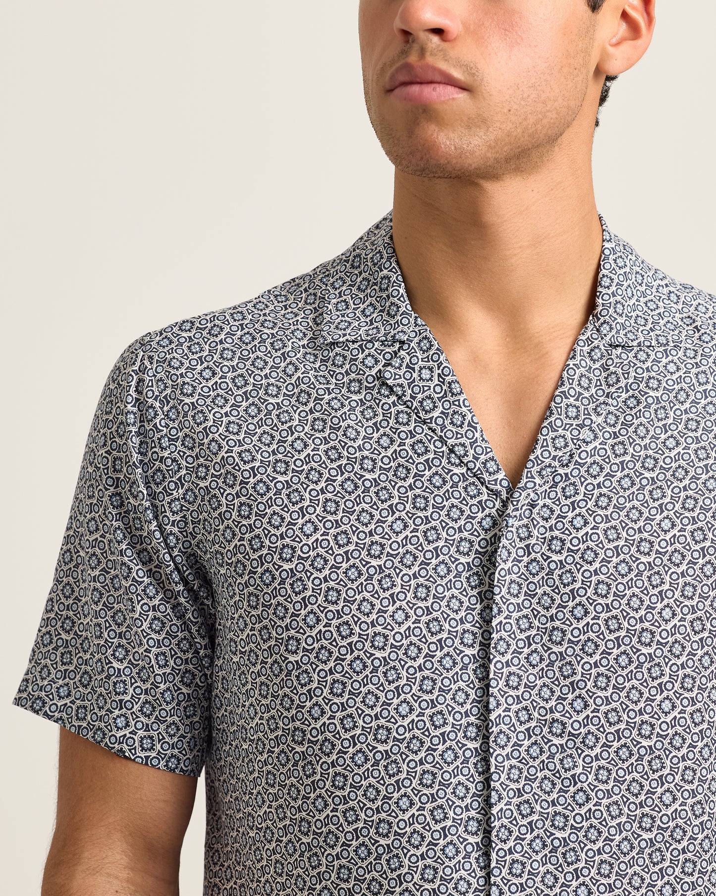 Man wearing a patterned short-sleeve shirt against a neutral background
