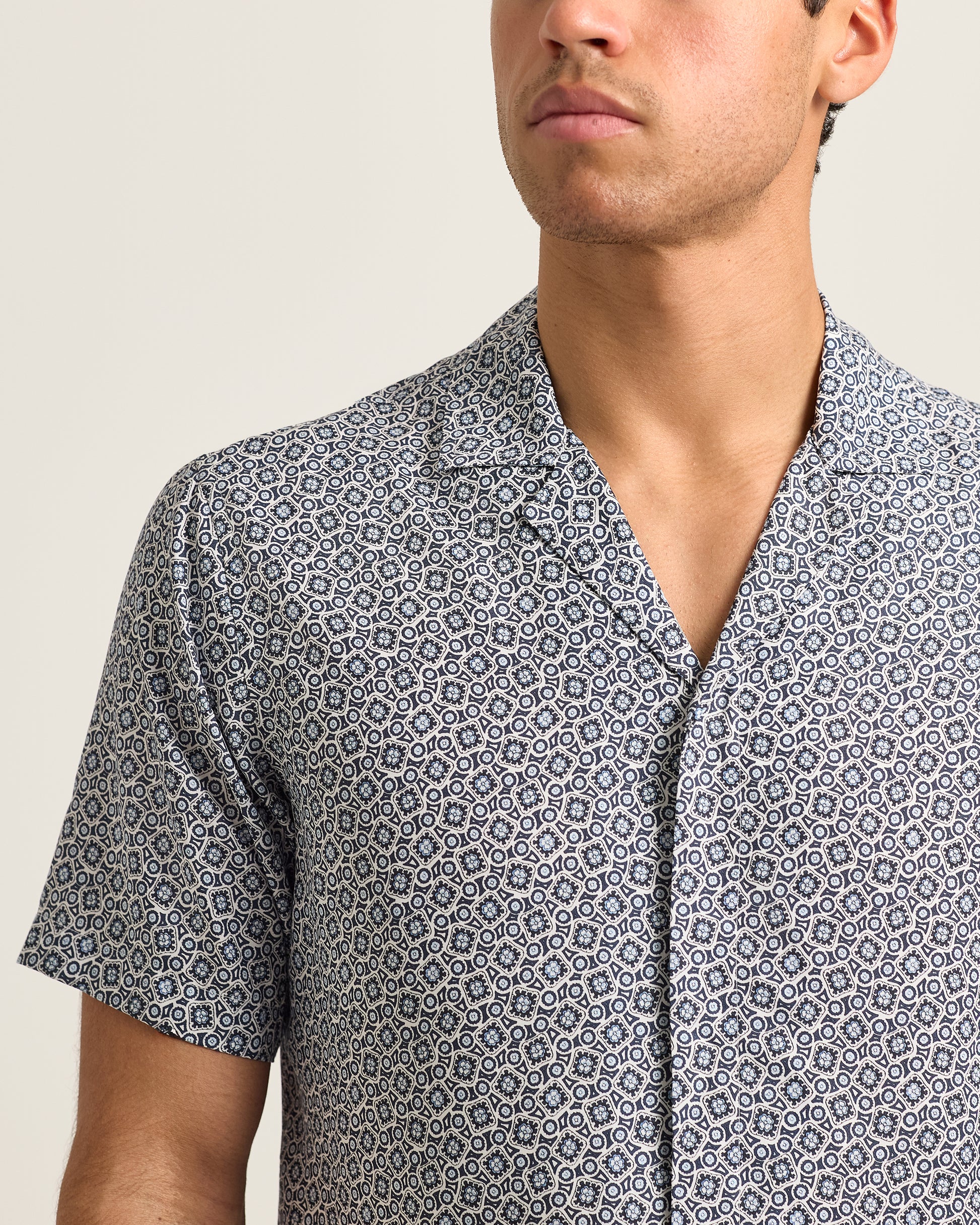 Man wearing a patterned short-sleeve shirt against a neutral background