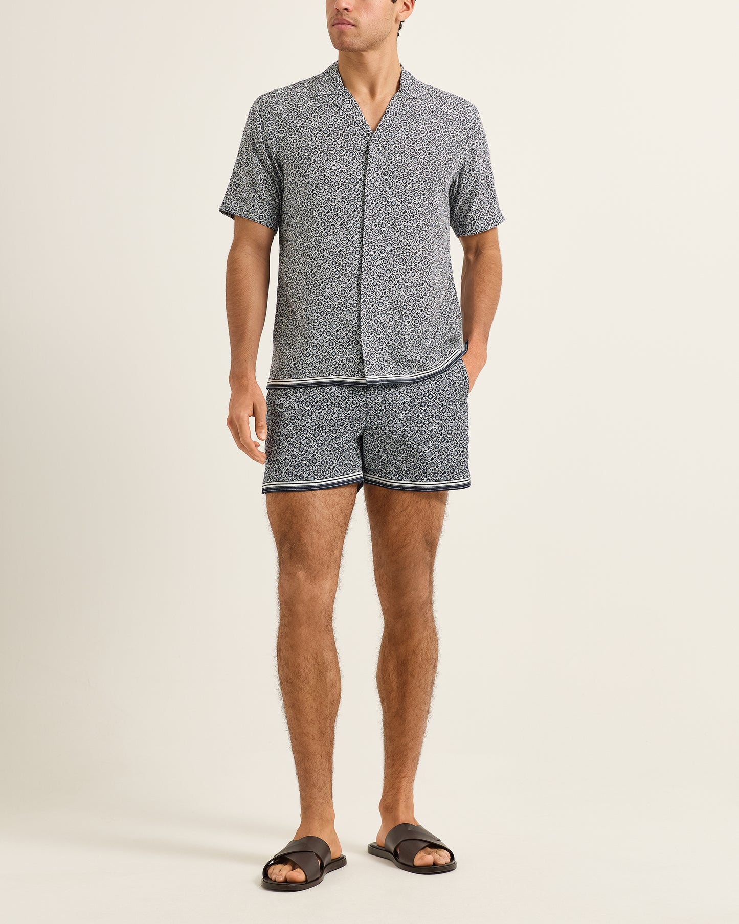 Man wearing a patterned shirt and shorts set on a beige background