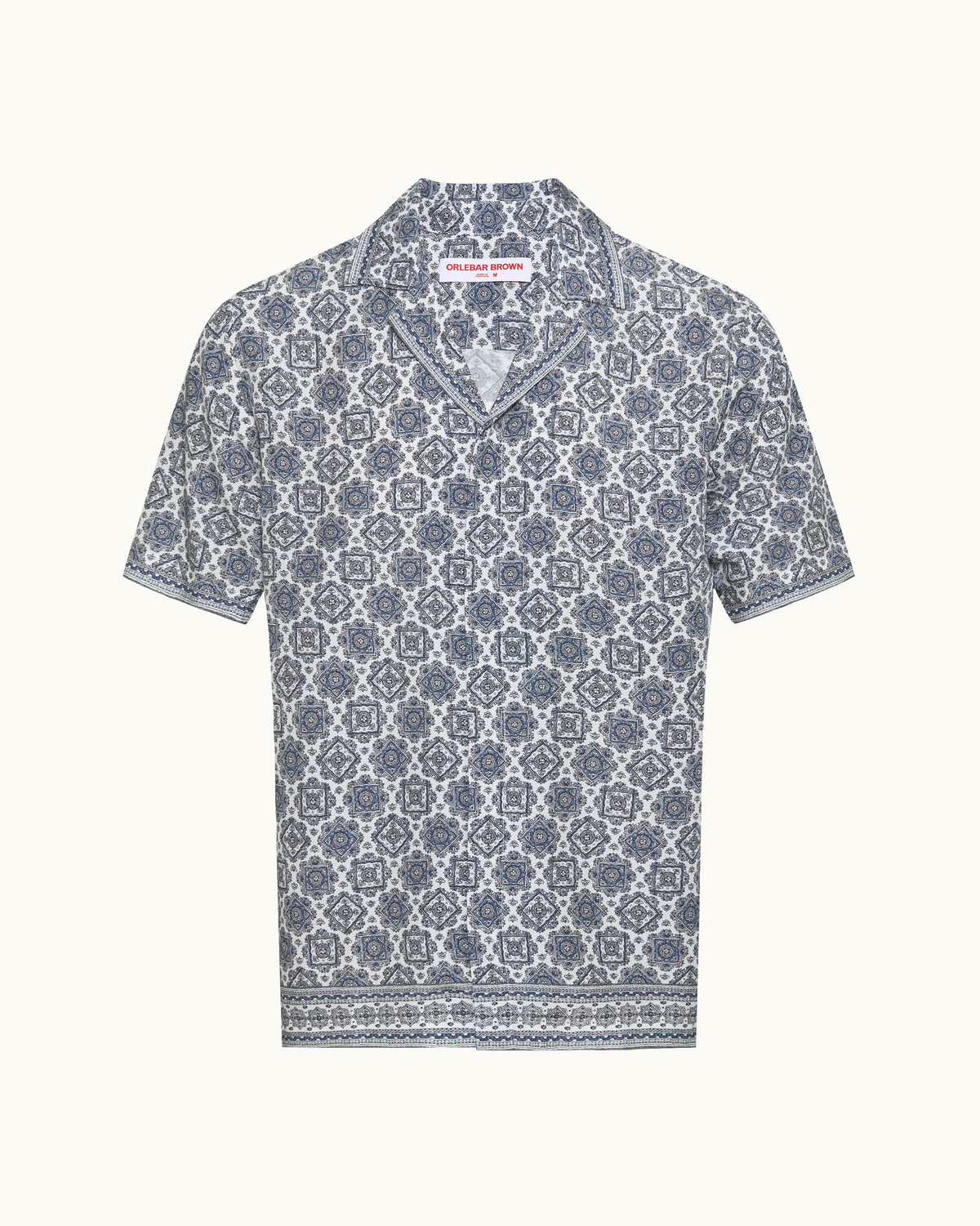 A short-sleeve button-up shirt with a blue and white geometric pattern, displayed flat against a light cream background.