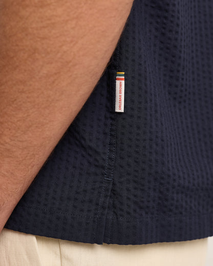 Navy blue textured shirt with a brand label on a neutral background