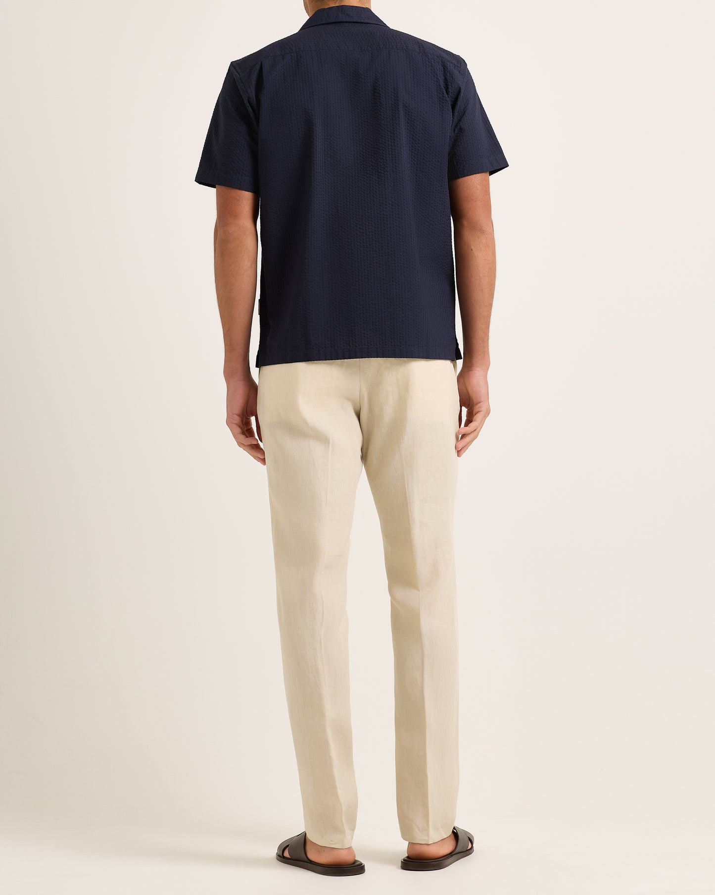 Model wearing navy short-sleeve shirt with beige trousers on a plain background 
