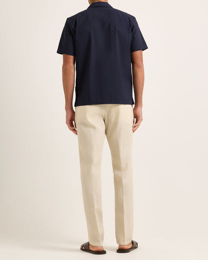 Model wearing navy short-sleeve shirt with beige trousers on a plain background 