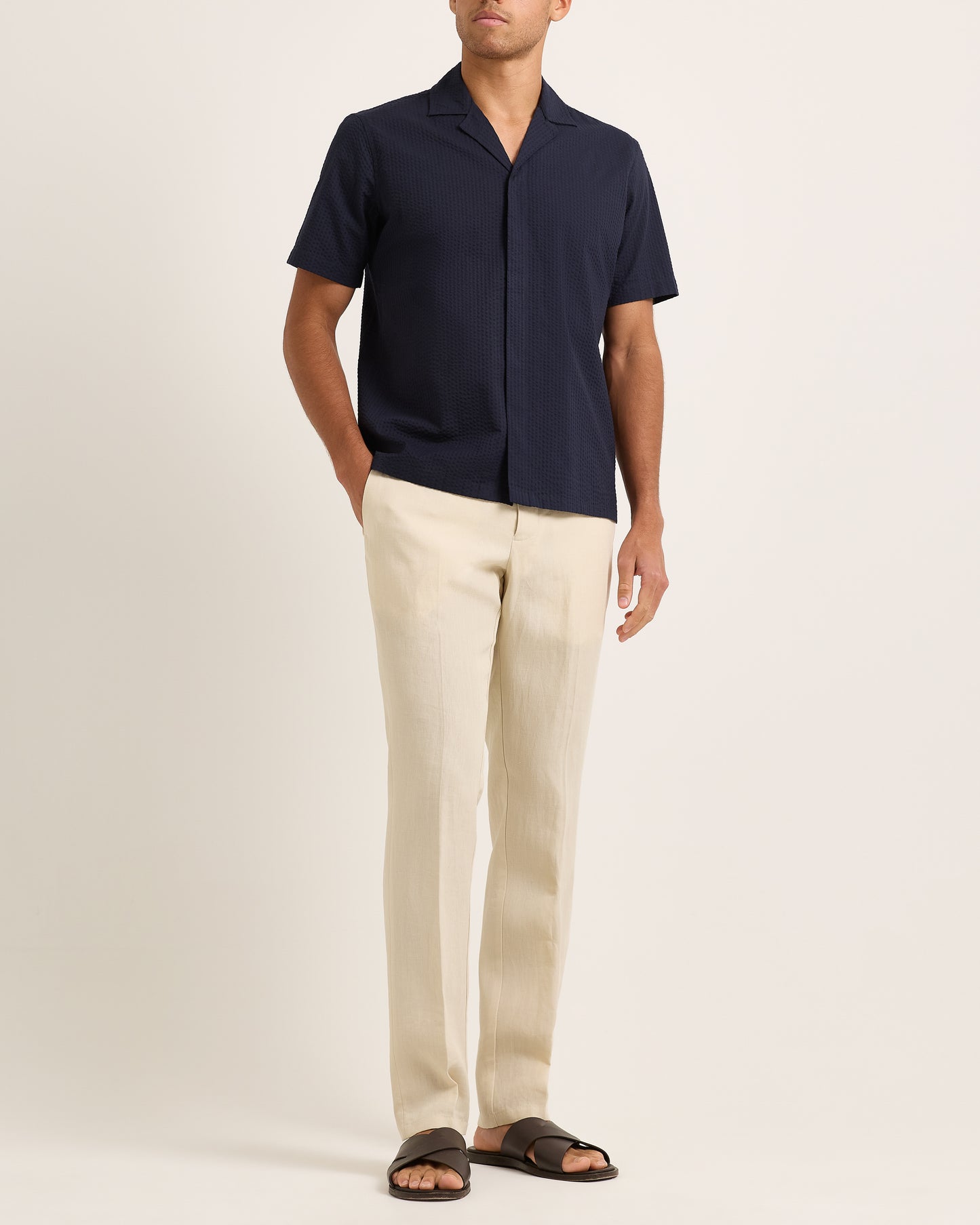 Model wearing navy short-sleeve shirt with beige trousers on a plain background 