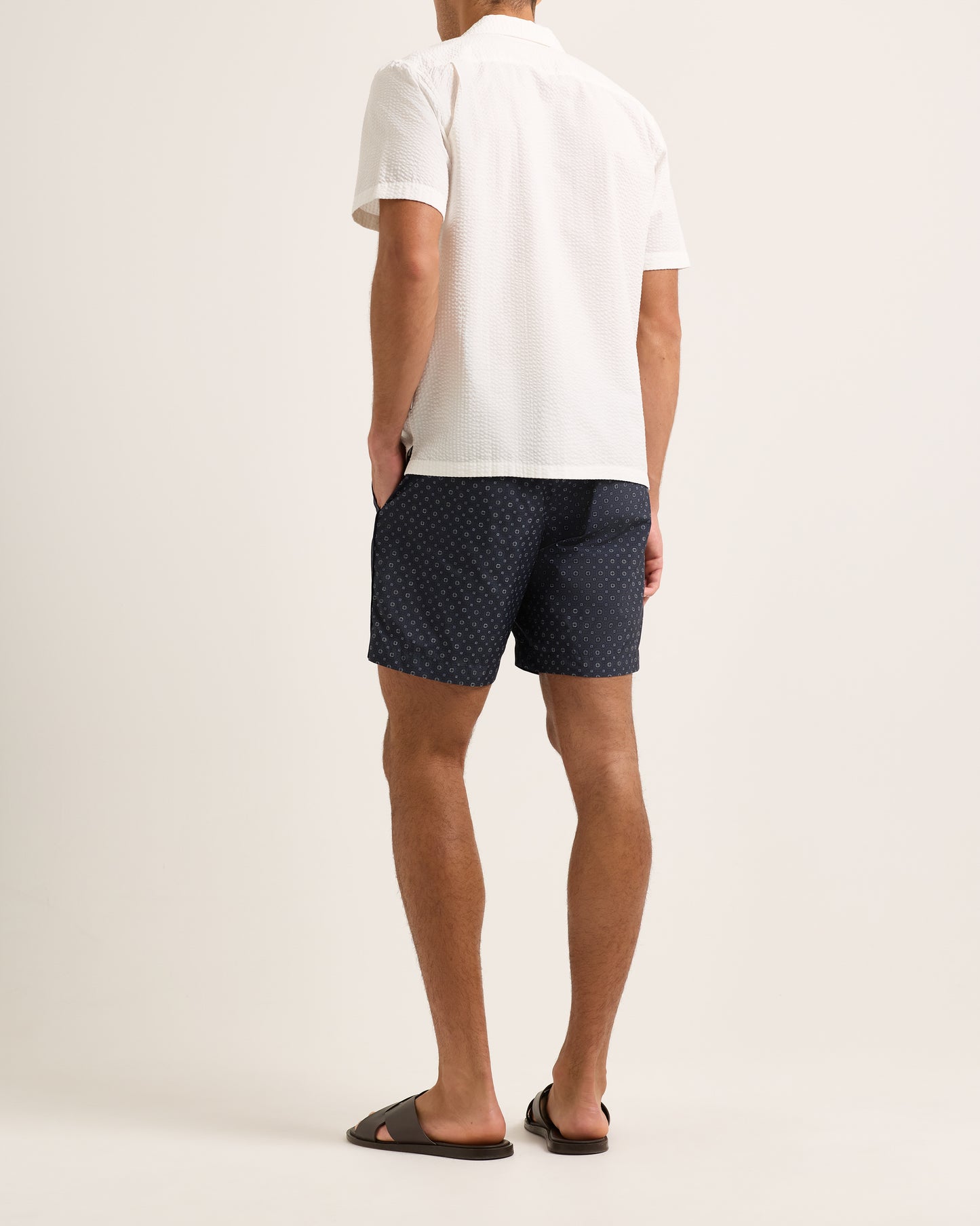Person wearing navy patterned shorts and a white shirt on a light background