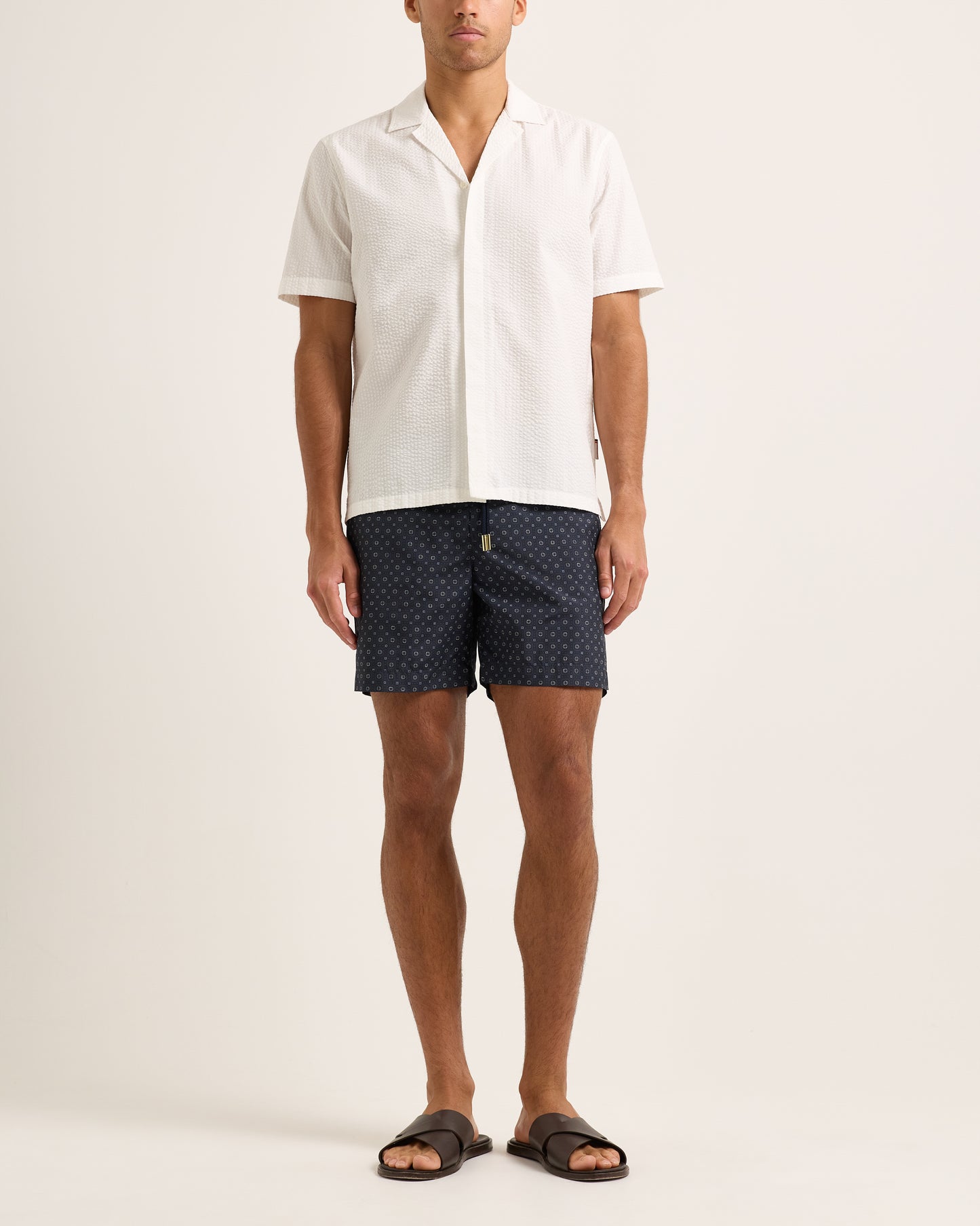 Person wearing navy patterned shorts and a white shirt on a light background