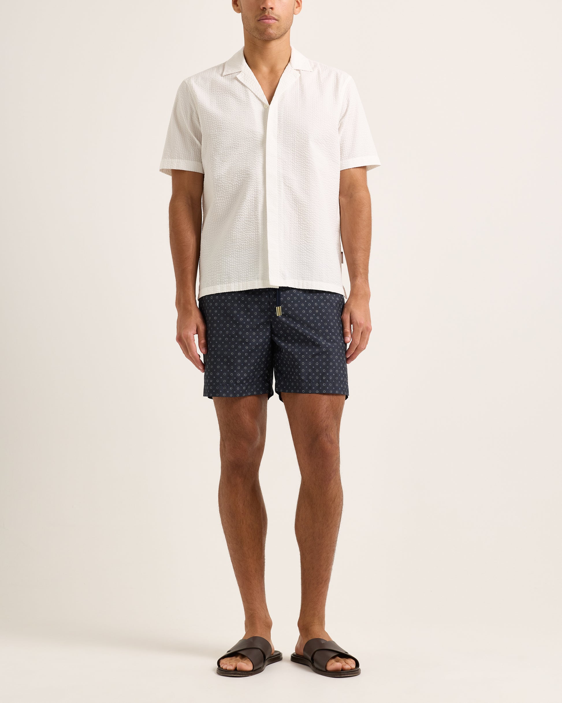 Person wearing navy patterned shorts and a white shirt on a light background