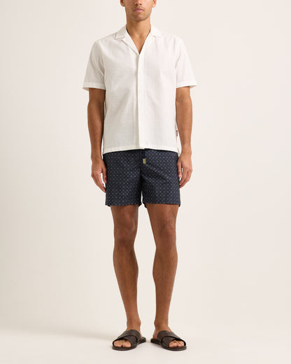 Person wearing navy patterned shorts and a white shirt on a light background