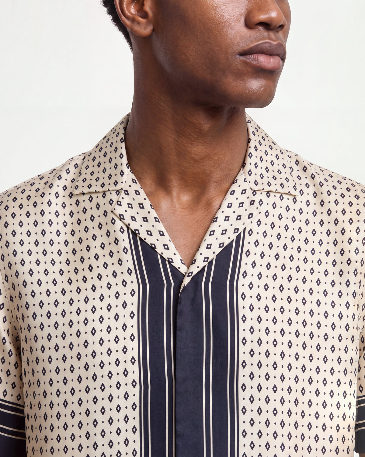 Close-up of a man wearing a beige patterned silk short-sleeved shirt with navy trim on a white background