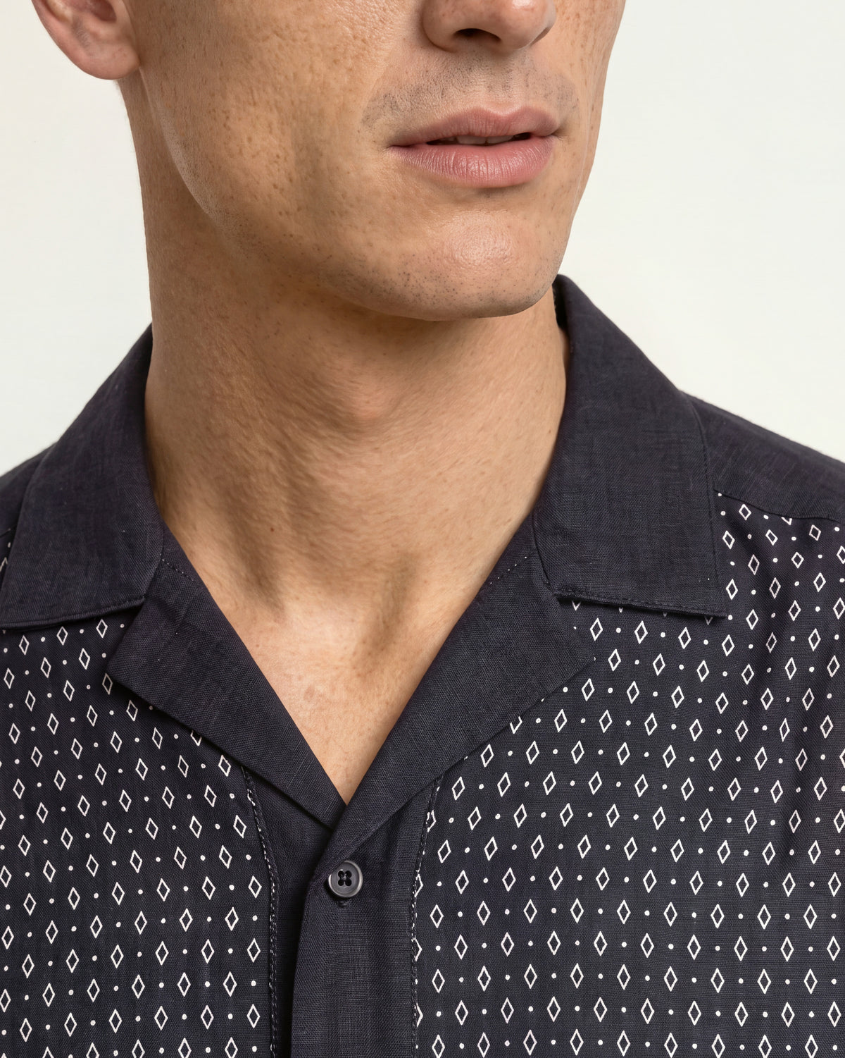 Close-up of a man wearing a dark navy button-up shirt with a white geometric diamond pattern on the front panels and solid navy on the collar and lower body.