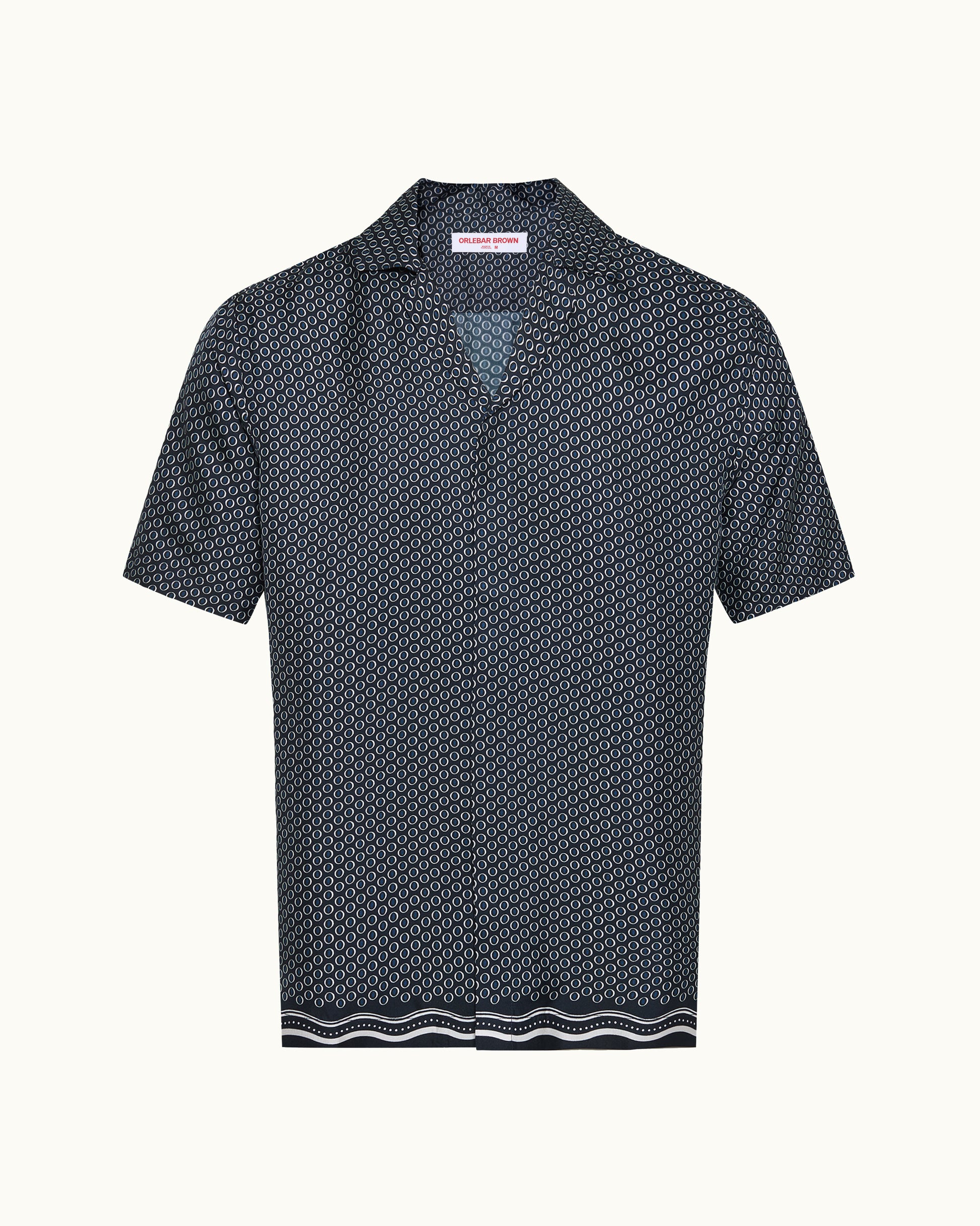 A short-sleeve collared shirt with a dense geometric micro-pattern in navy and white, featuring a striped border at the hem, shown against a plain off-white background.