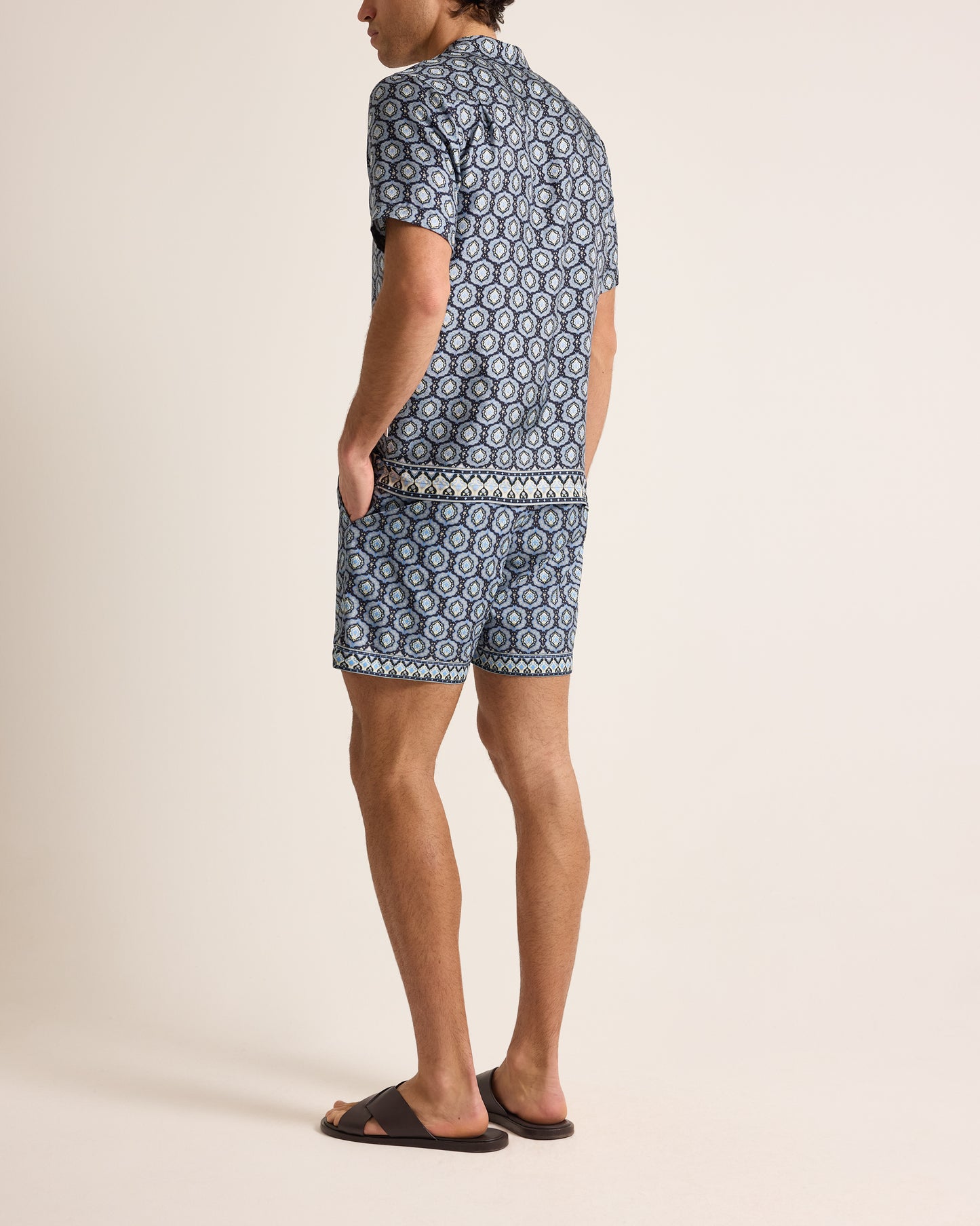 Person wearing a blue patterned shirt and shorts on a beige background