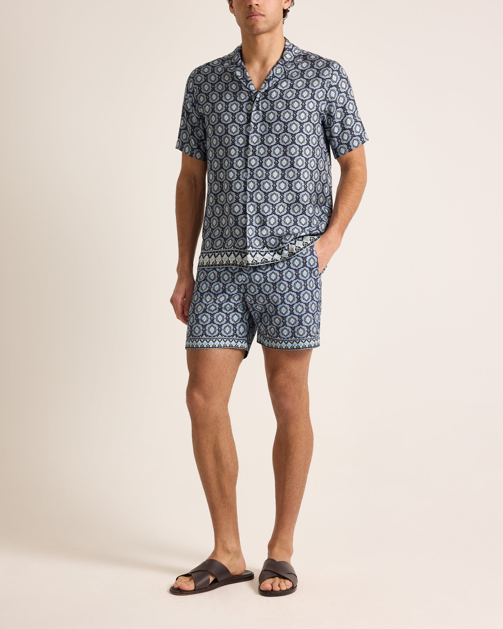 Man wearing a navy patterned shirt and shorts set on a beige background
