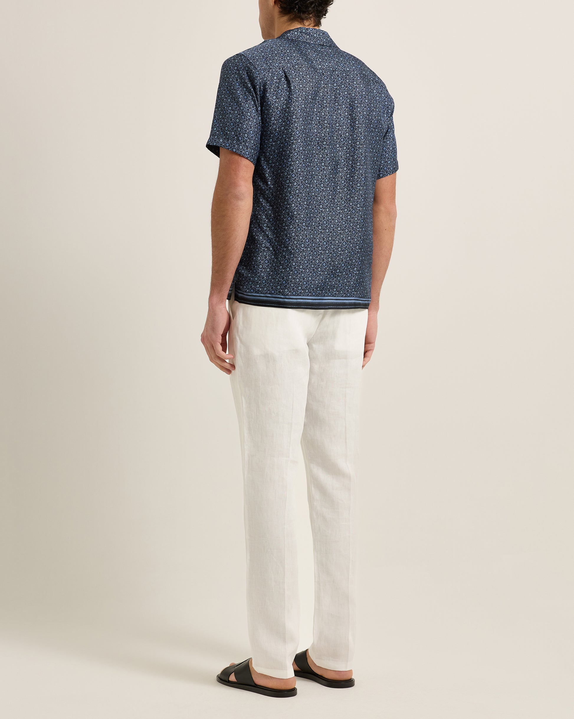 Person wearing a blue patterned shirt and white pants on a plain background