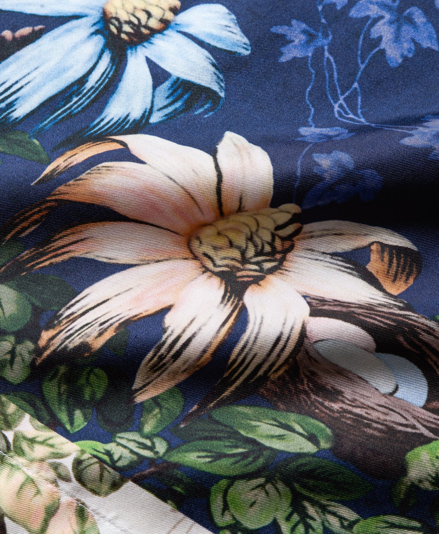 A close-up of a floral fabric print featuring a large cream flower with black outlines, green leaves, and a blue flower on a dark navy background.