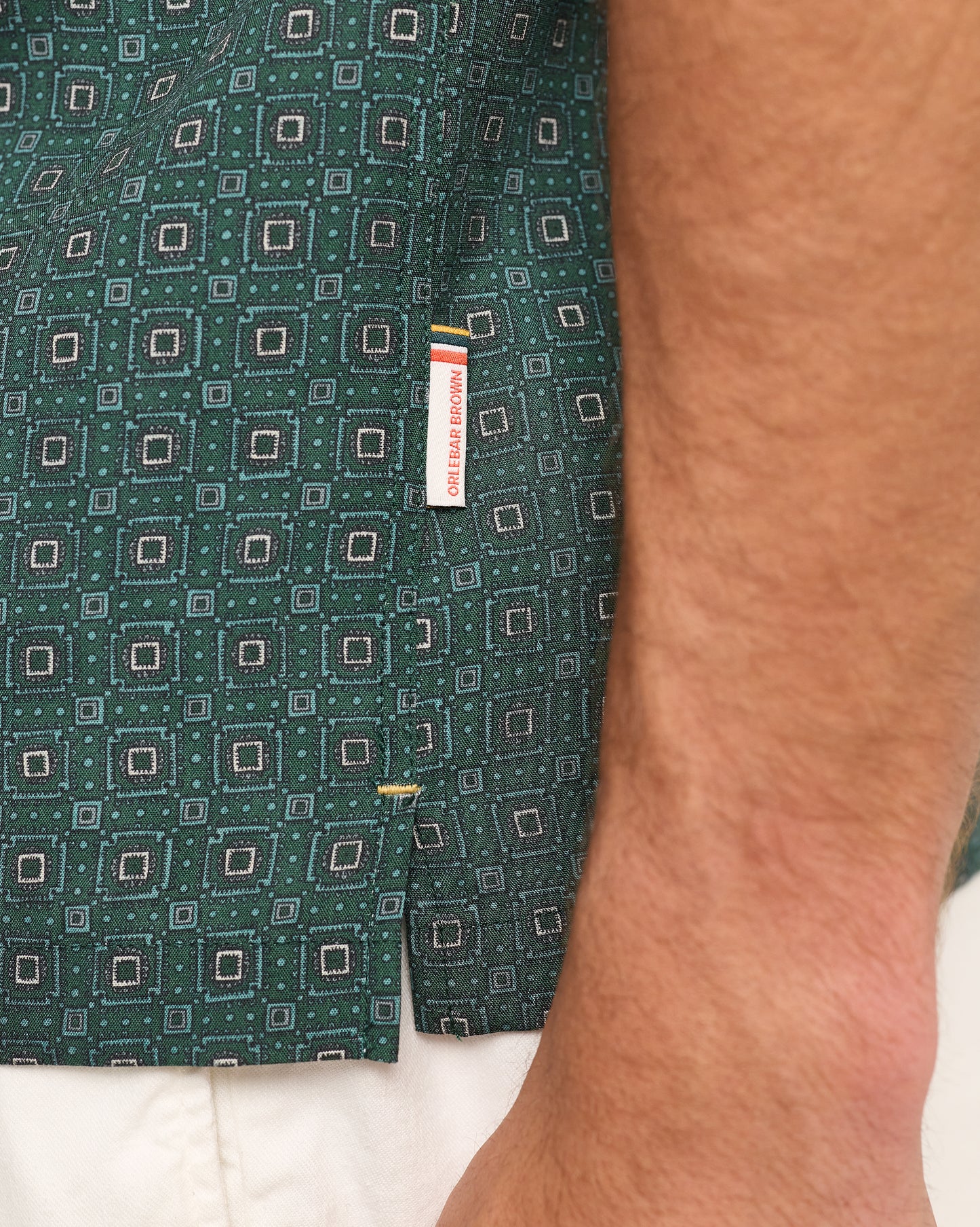 Close-up of model wearing dark green patterned with branding label on a white background