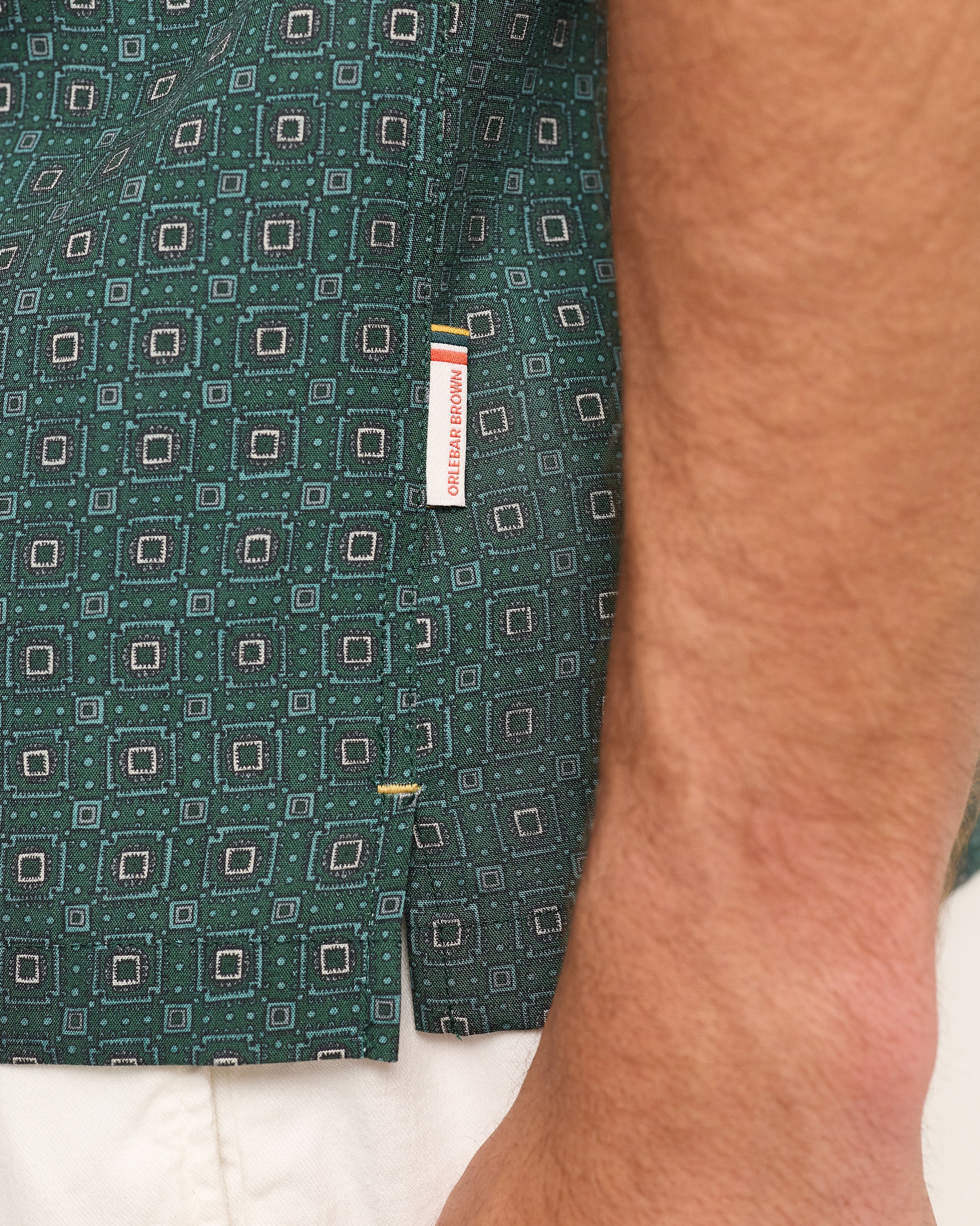 Close-up of model wearing dark green patterned with branding label on a white background