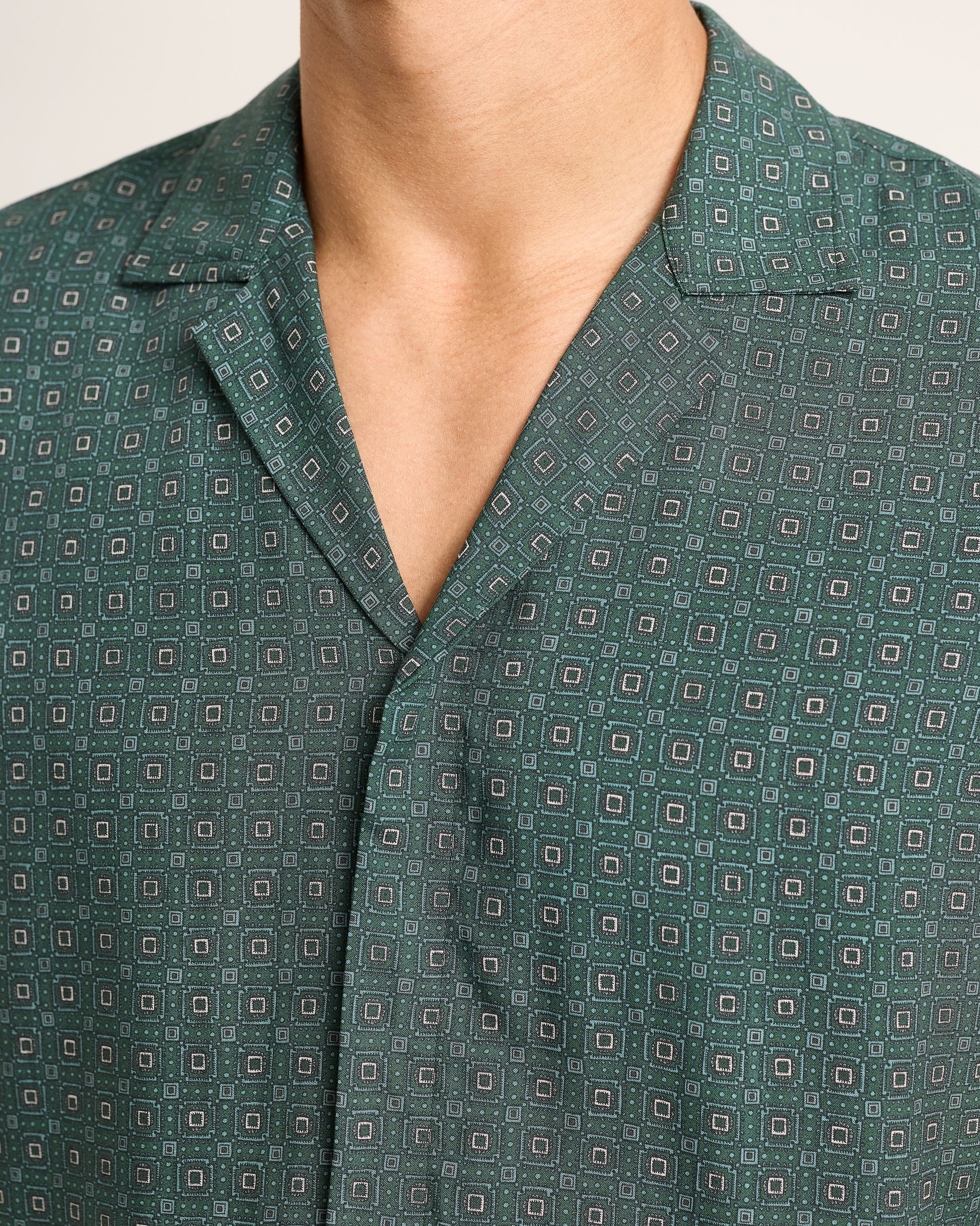 Close-up of model wearing dark green patterned short-sleeve shirt on a white background