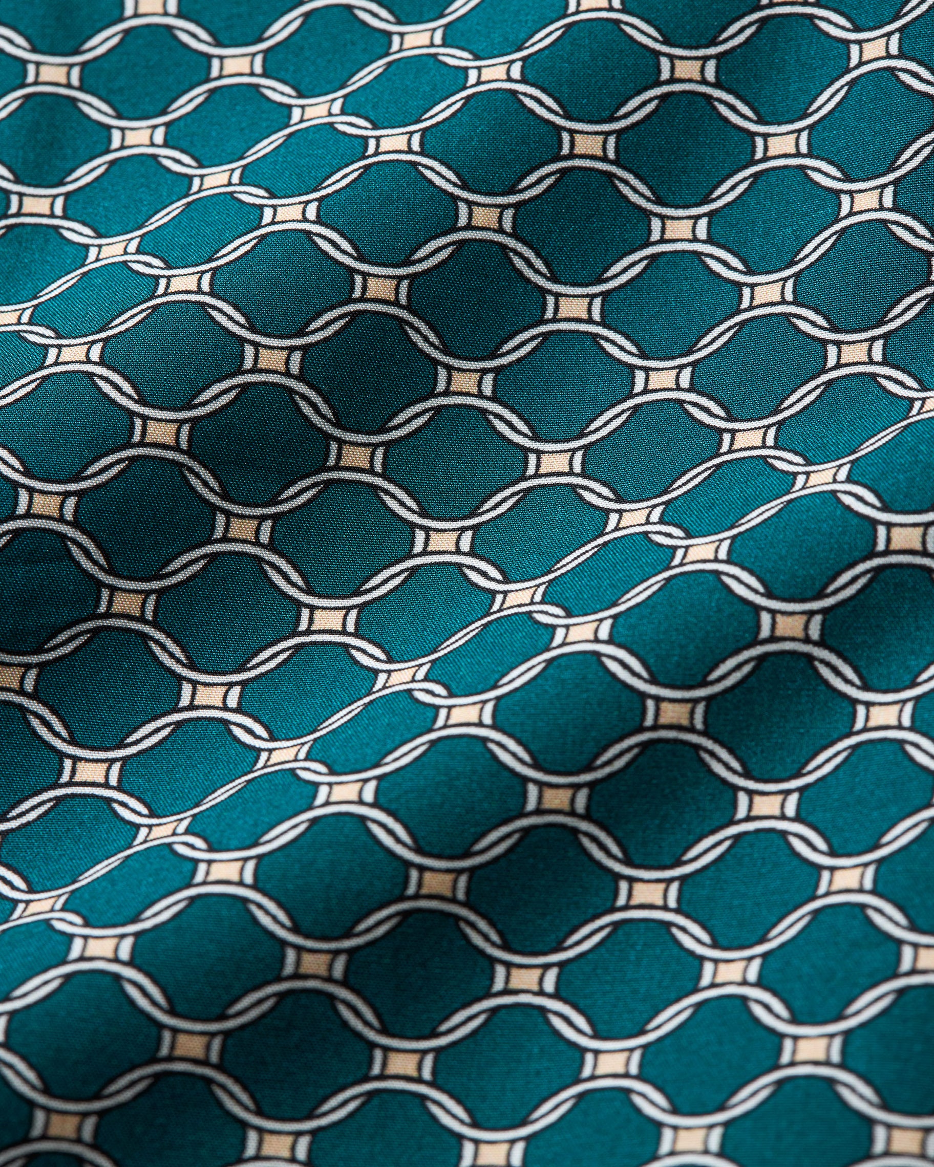 A close-up of a teal fabric with a repeating cream geometric lattice pattern.