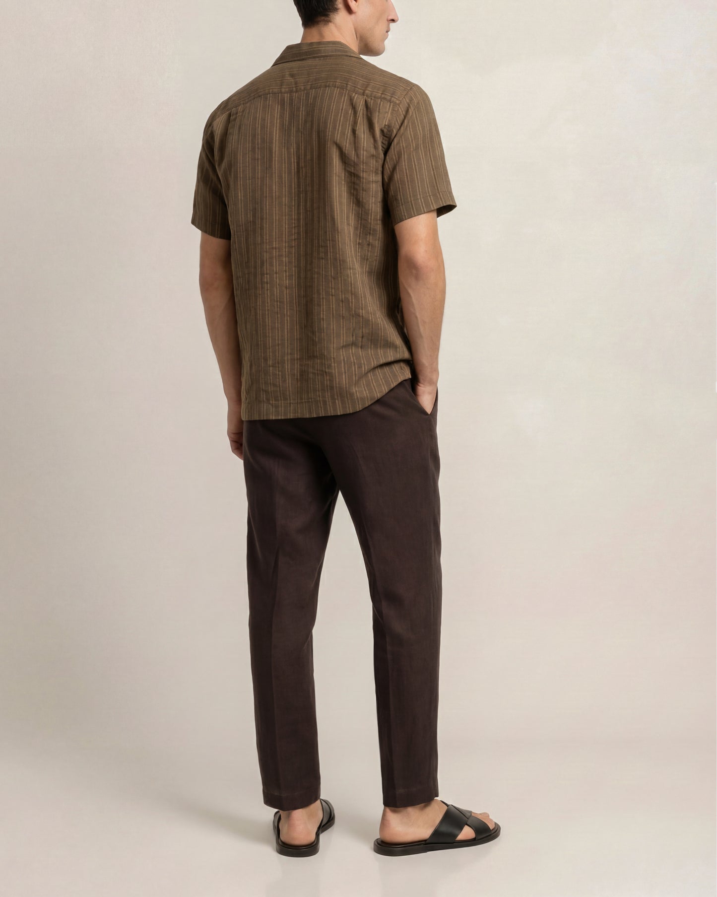 Man wearing a brown checkered shirt and dark pants on a plain background