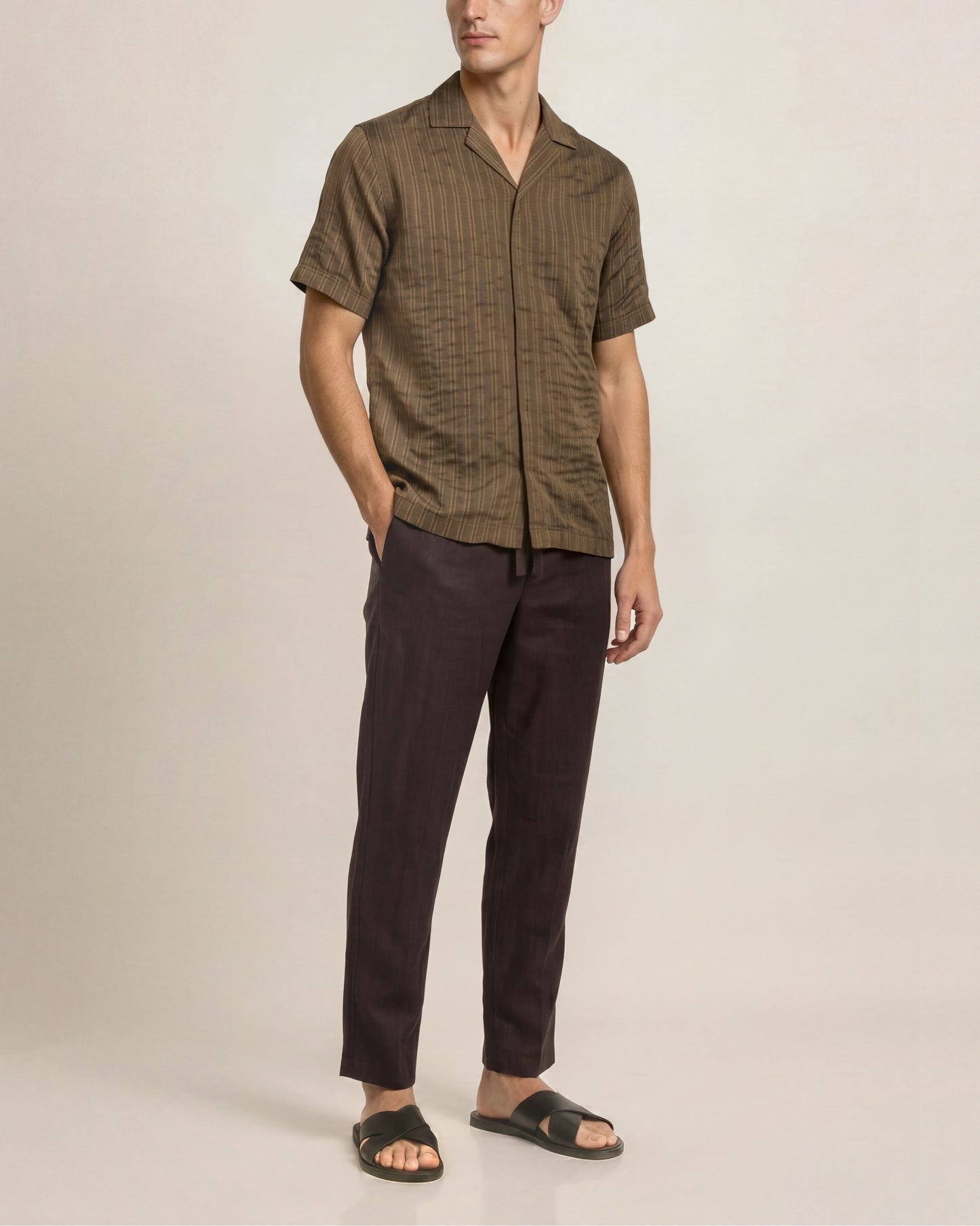 Man wearing a brown checkered shirt and dark pants on a beige background
