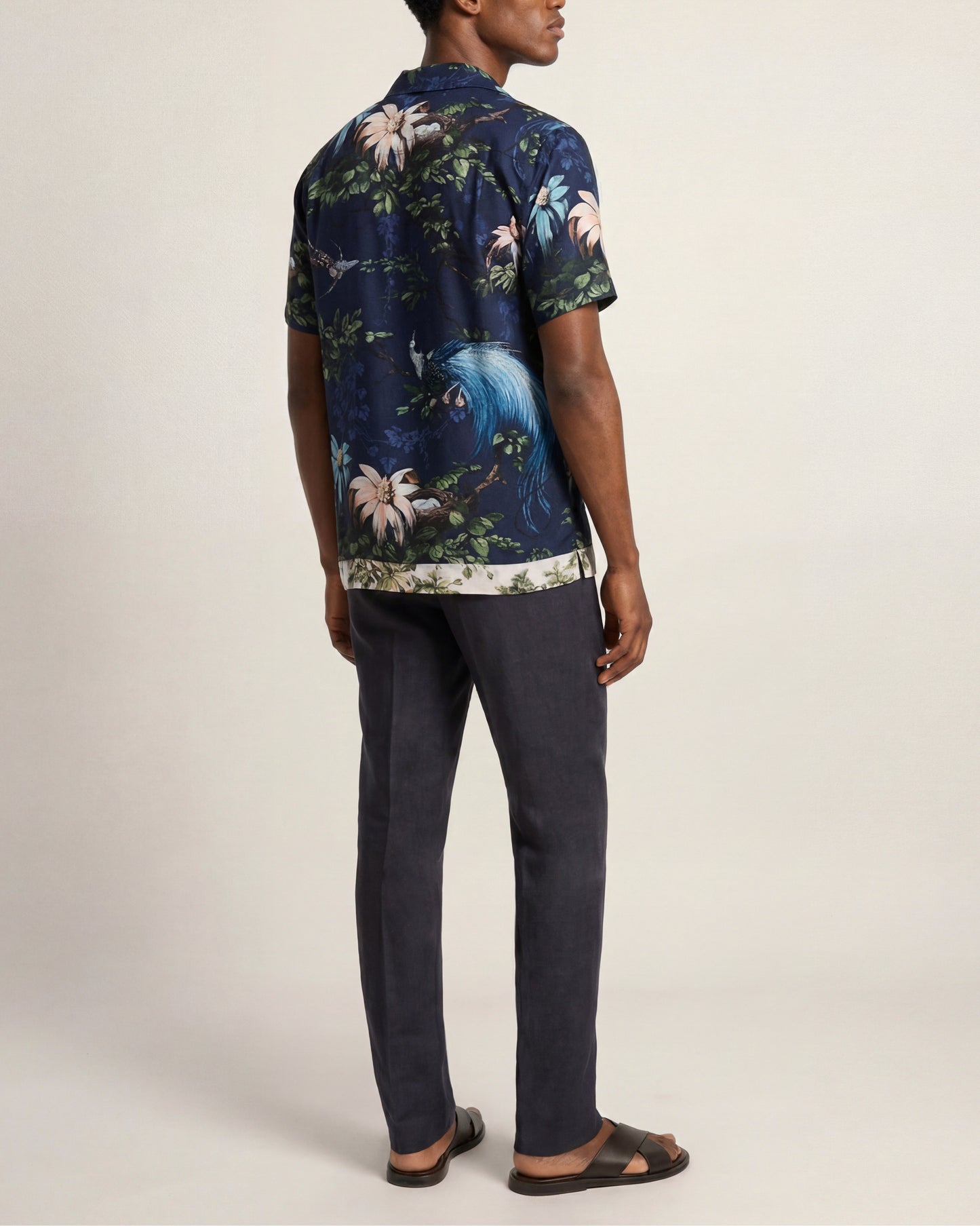Person wearing a dark floral shirt and dark pants on a plain background
