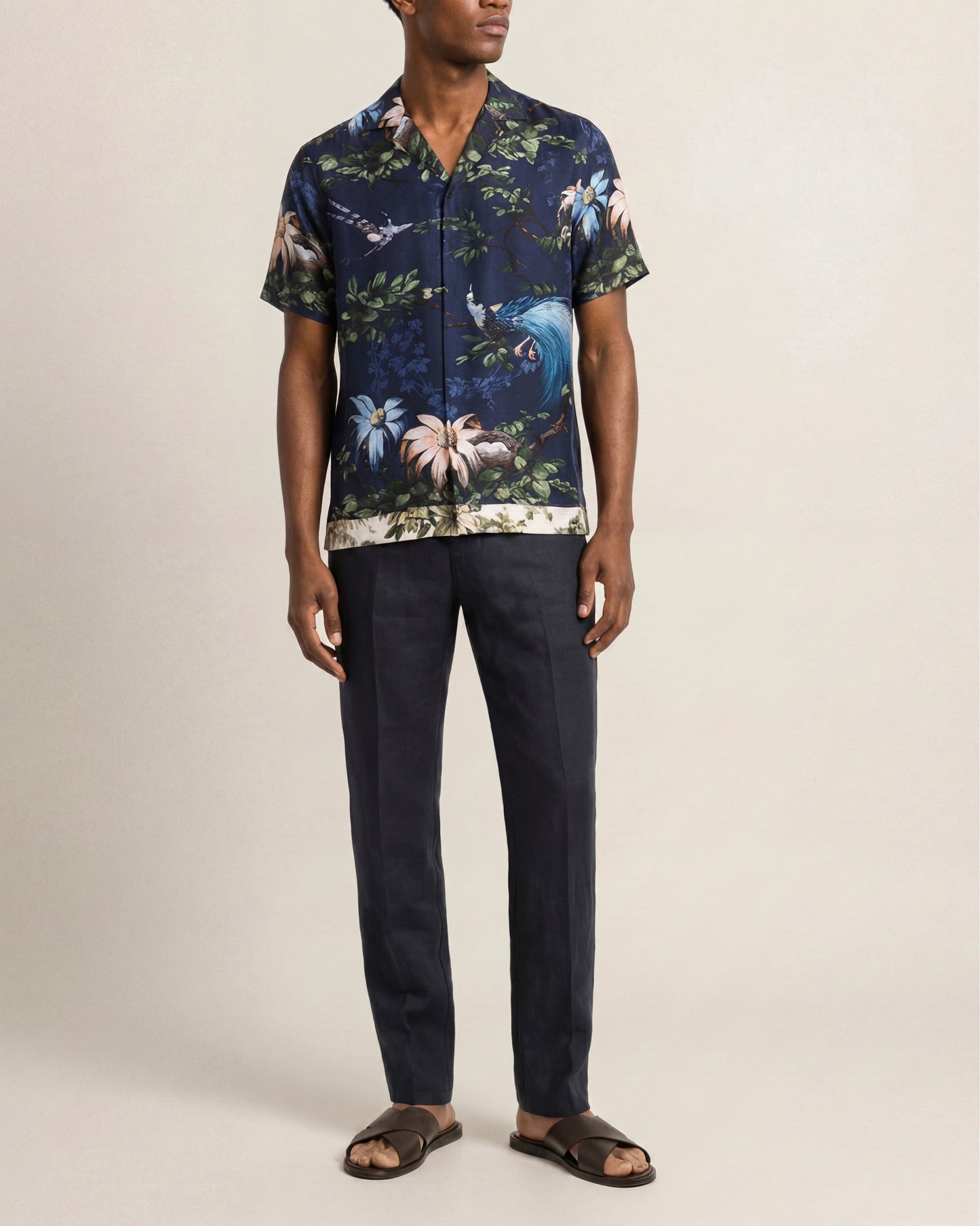 Man wearing a dark blue floral shirt and black pants on a beige background