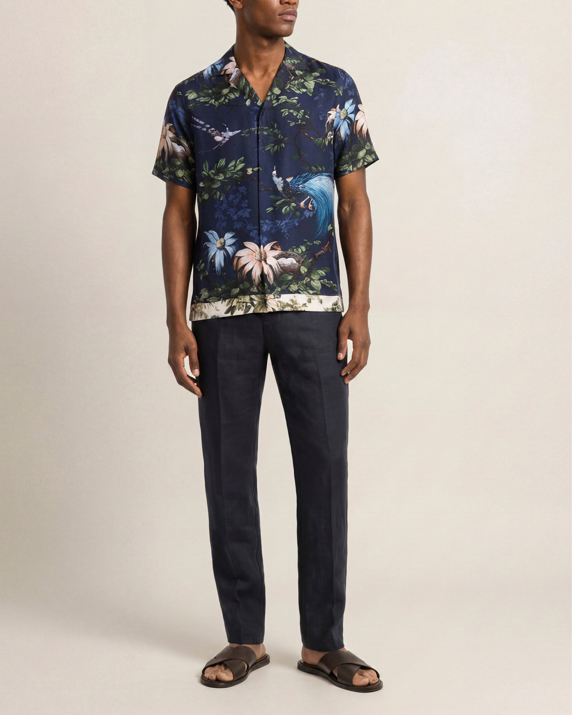 Man wearing a dark blue floral shirt and black pants on a beige background