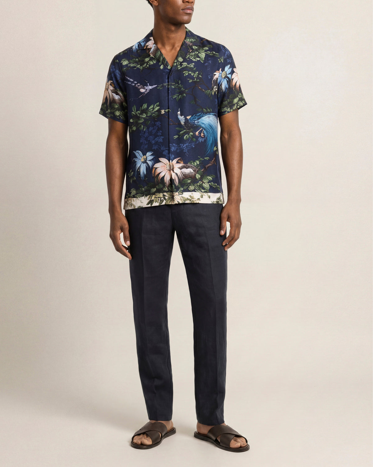 Man wearing a dark blue floral shirt and black pants on a beige background
