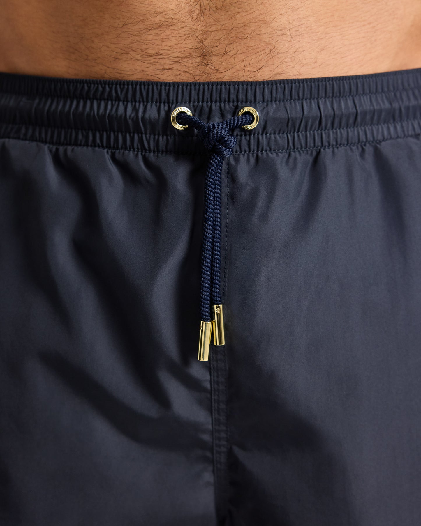 Navy swim shorts with drawstring and metal buckle on a neutral background