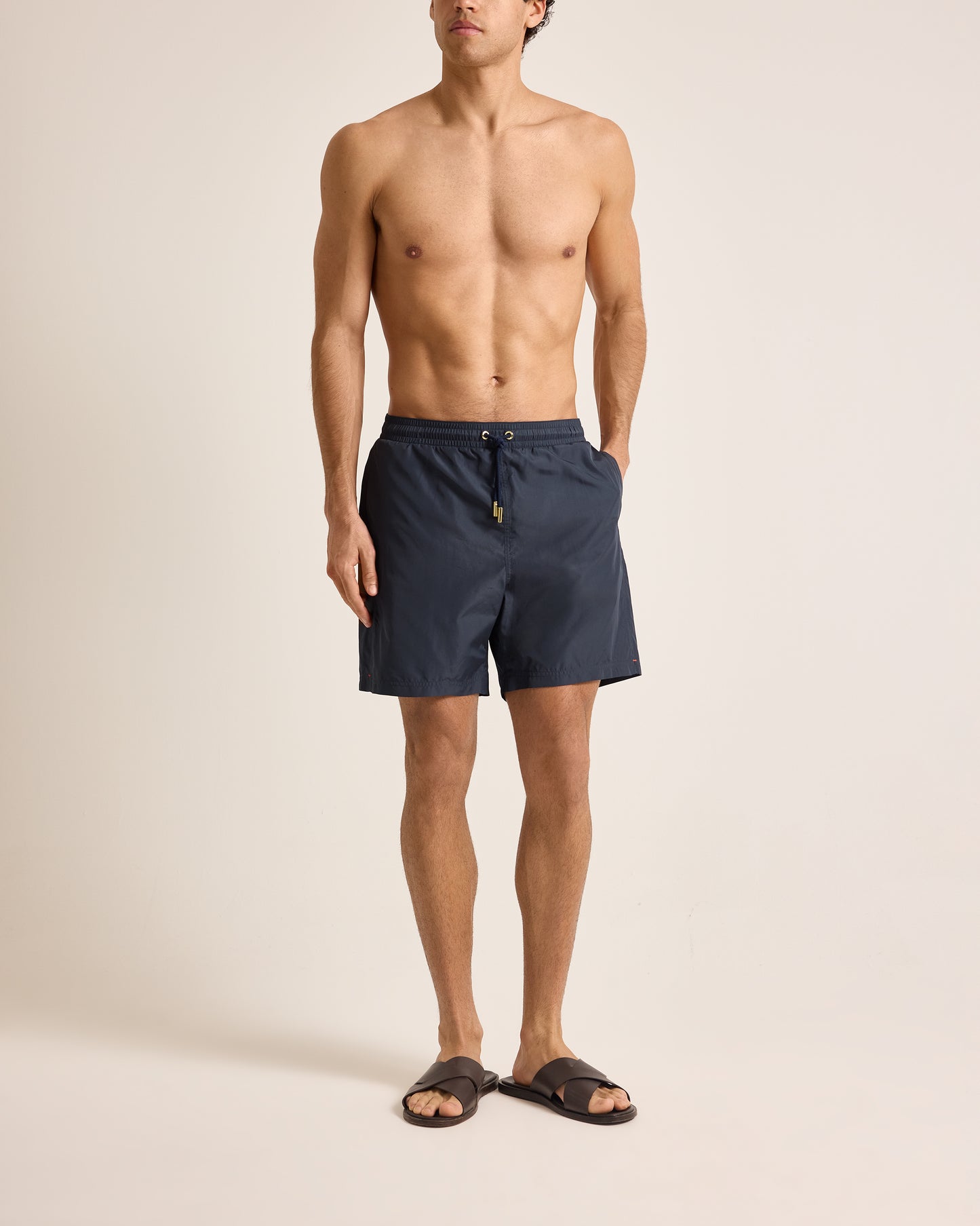 Man wearing navy blue swim shorts on a beige background