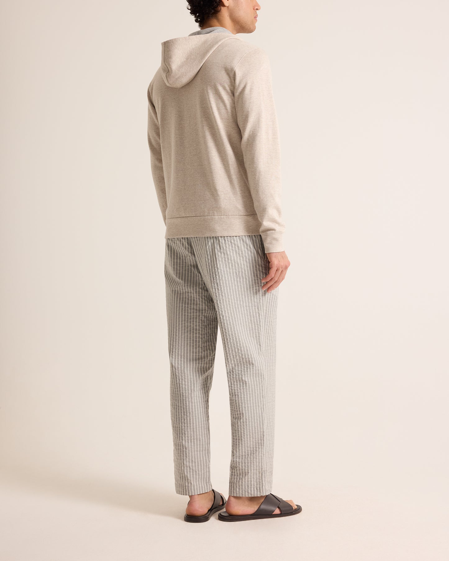 Person wearing a beige hoodie and striped pants on a plain background