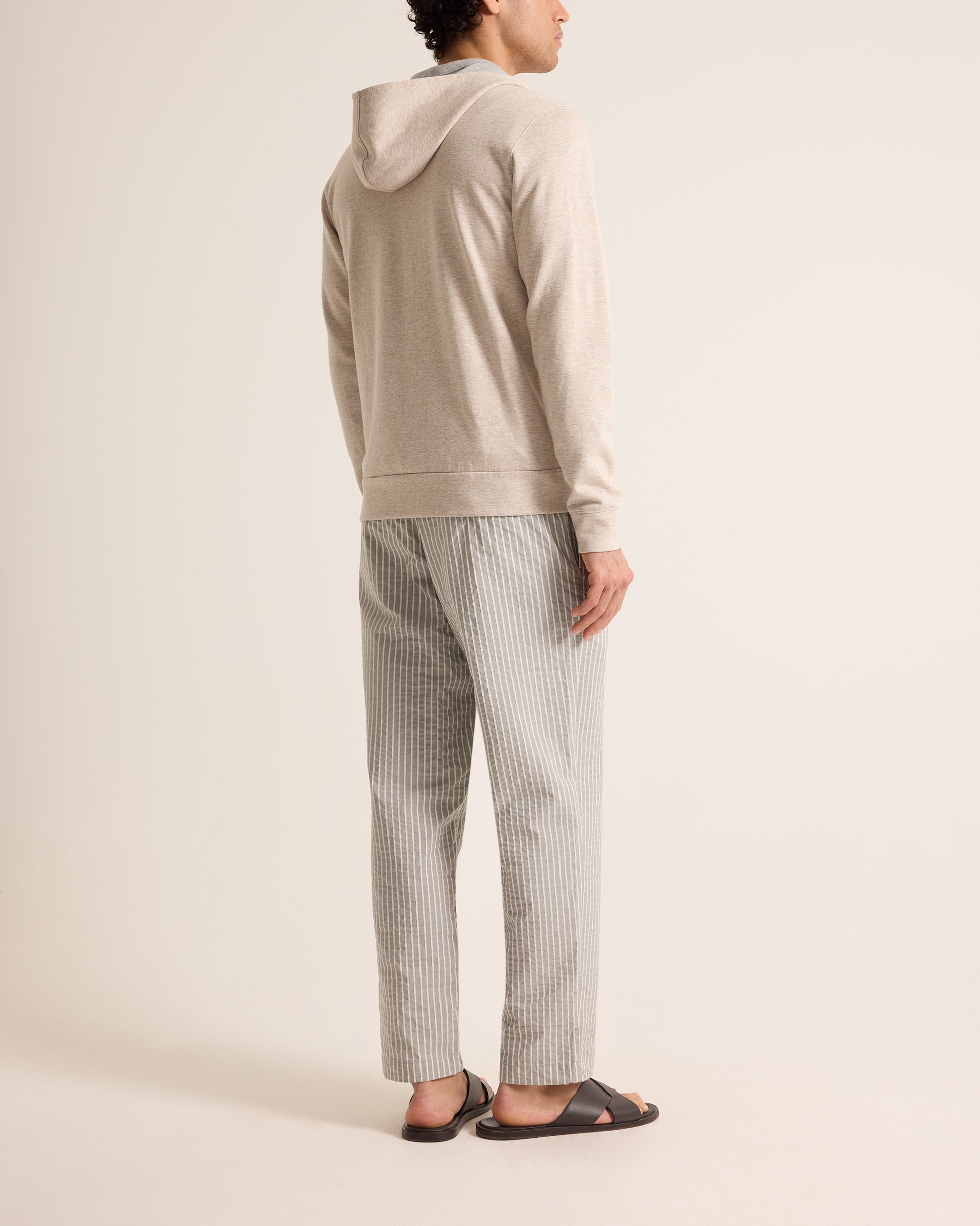 Person wearing a beige hoodie and striped pants on a plain background