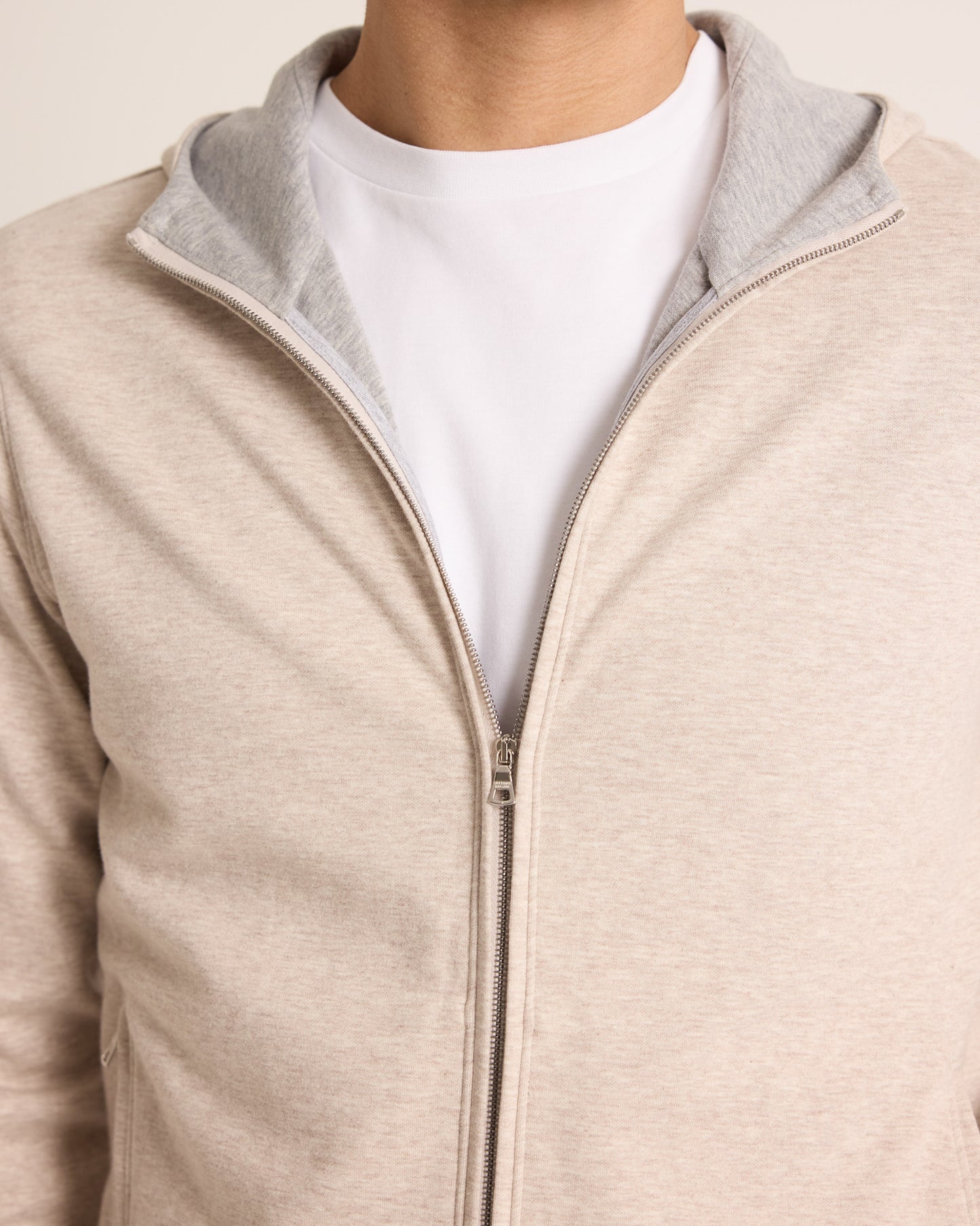 Close-up of a beige zip-up jacket with gray lining worn over a white shirt.