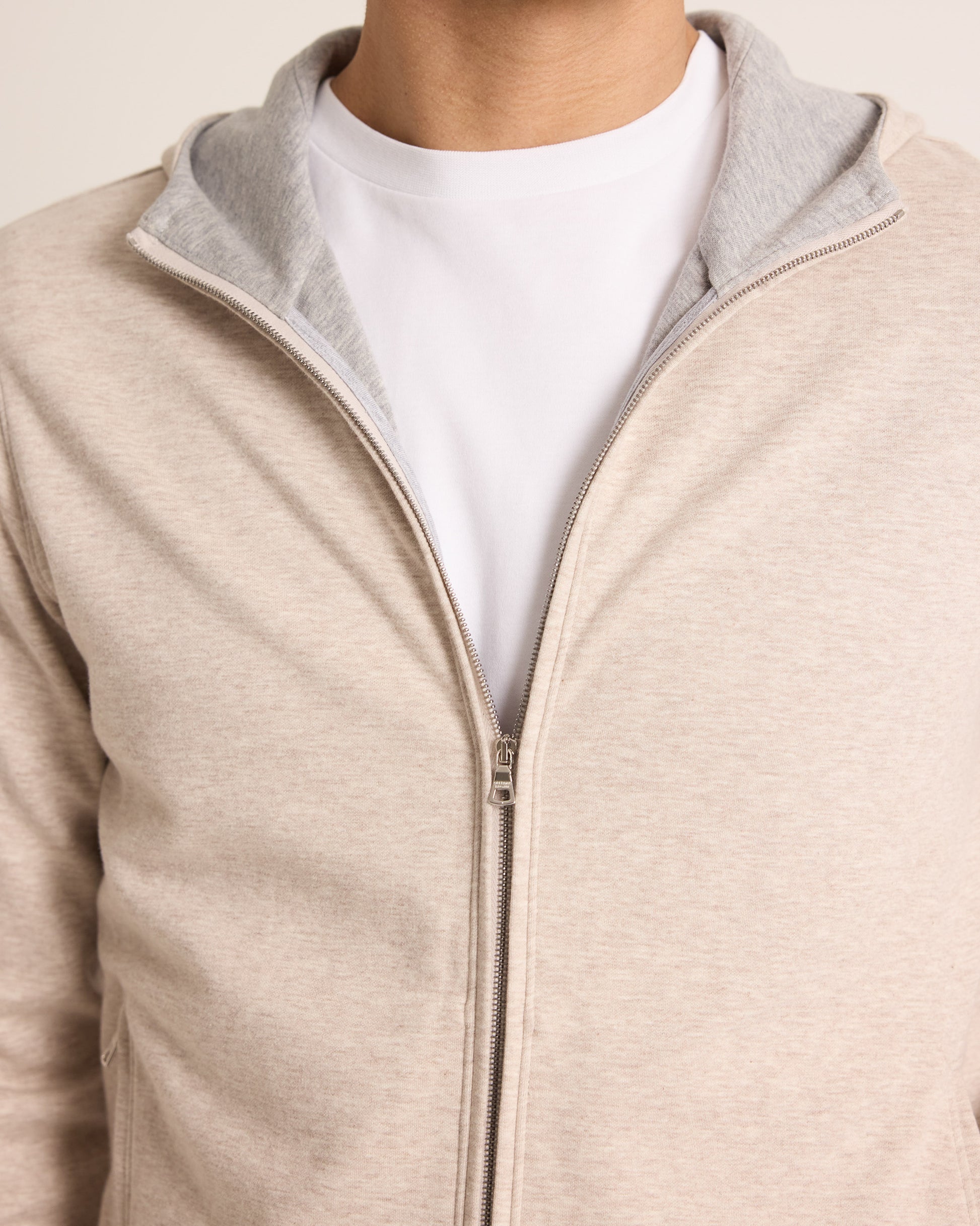 Close-up of a beige zip-up jacket with gray lining worn over a white shirt.