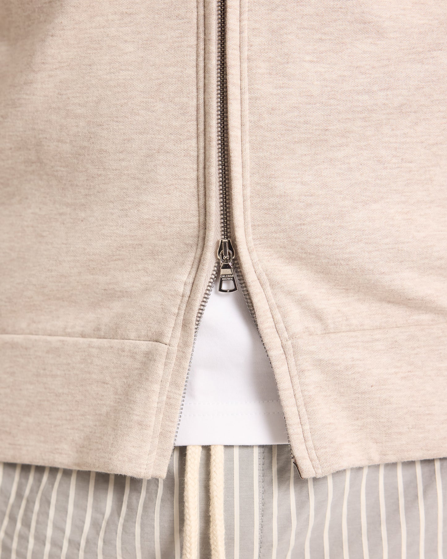 Close-up of a beige zip-up hoodie with a white shirt underneath.