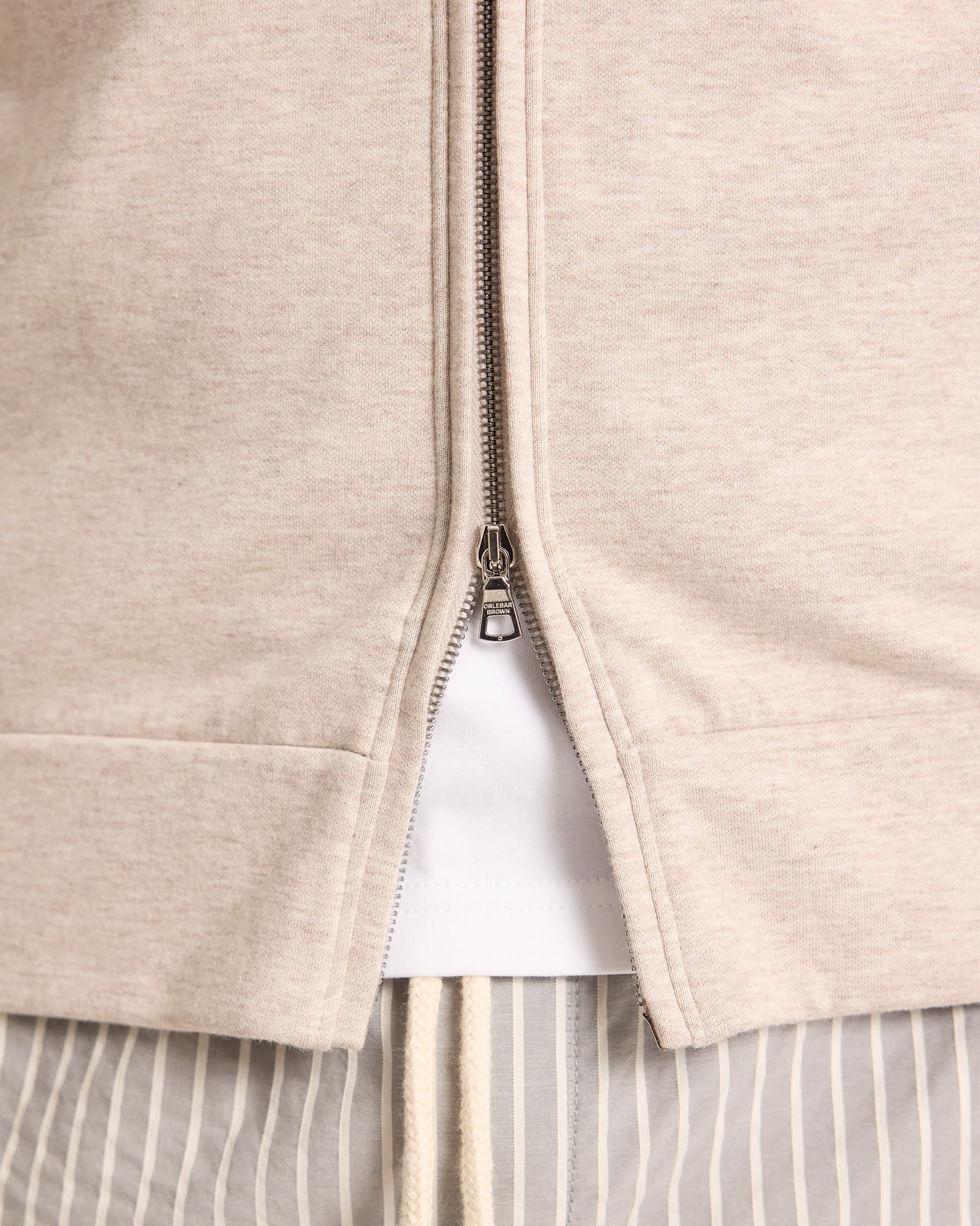 Close-up of a beige zip-up hoodie with a white shirt underneath.