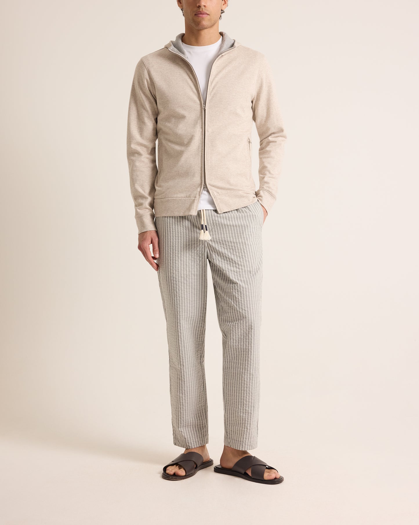 Man wearing a beige zip-up jacket, white shirt, and gray checkered pants on a plain background